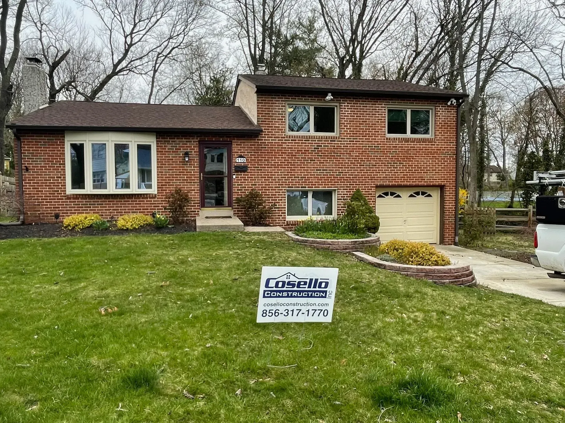 Brick house with brown roof, bay window, and a sign on the lawn.