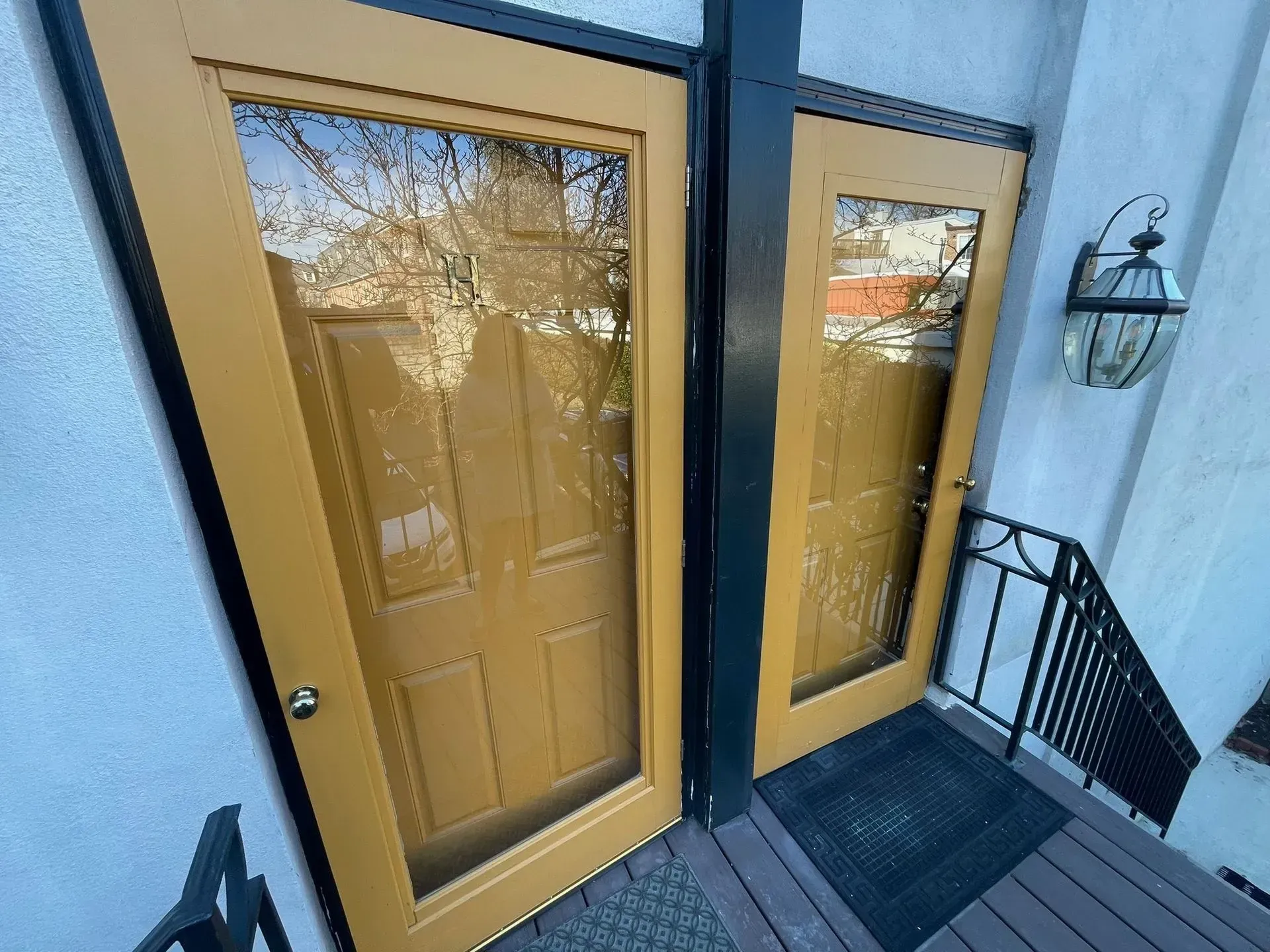 Two golden doors with glass panels on a small porch, with a black metal railing and lantern.