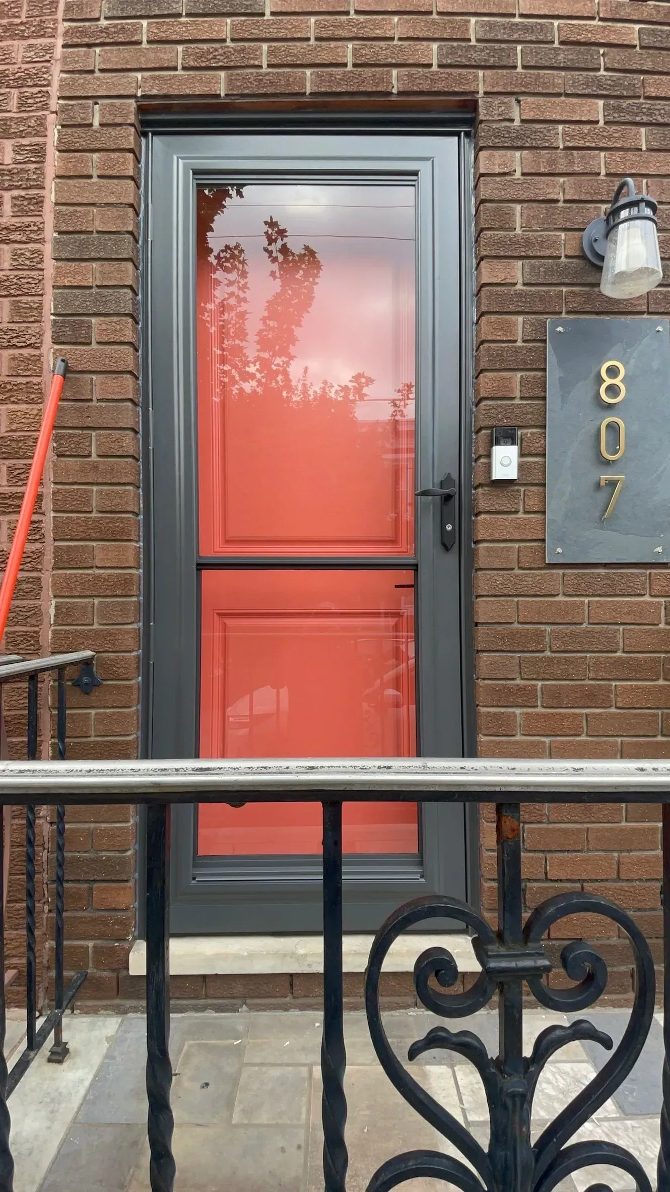 Red door framed by a gray storm door, brick wall, and wrought iron railing. House number is 807.