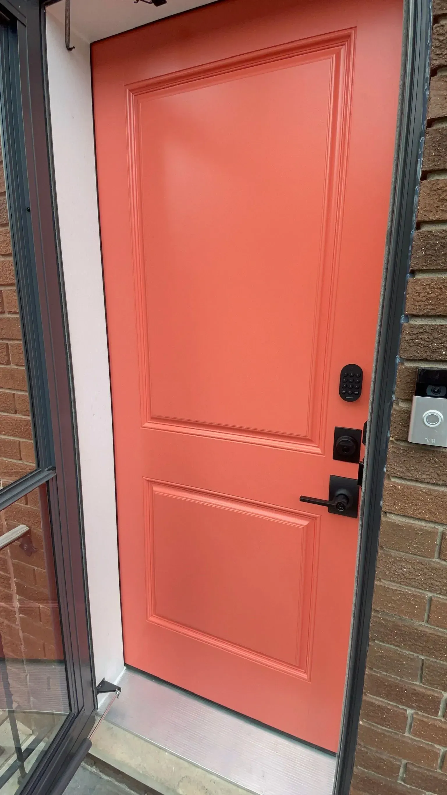 Coral front door with black hardware, brick exterior.