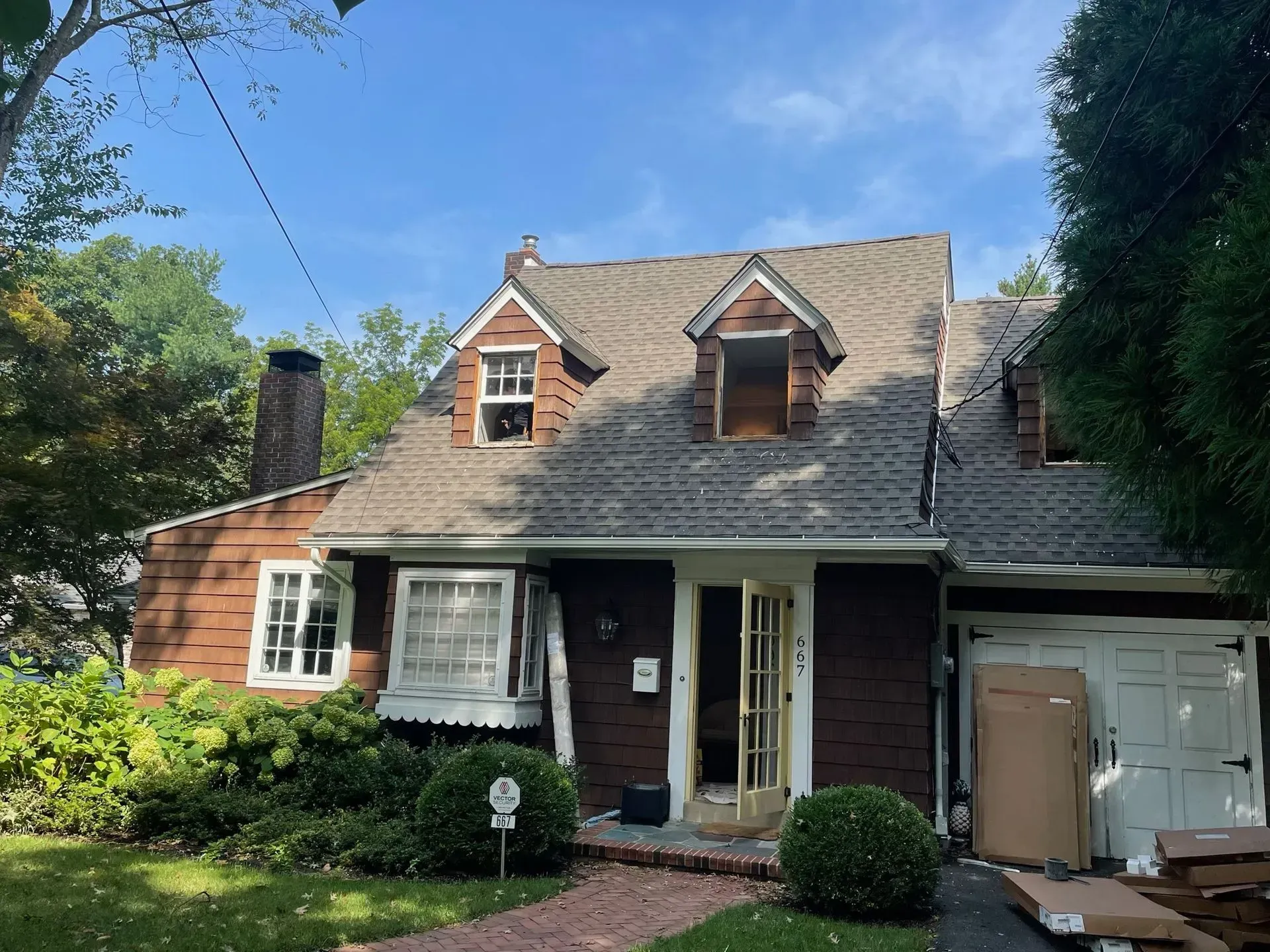Brown house with a brick walkway and open door under a blue sky, construction materials present.