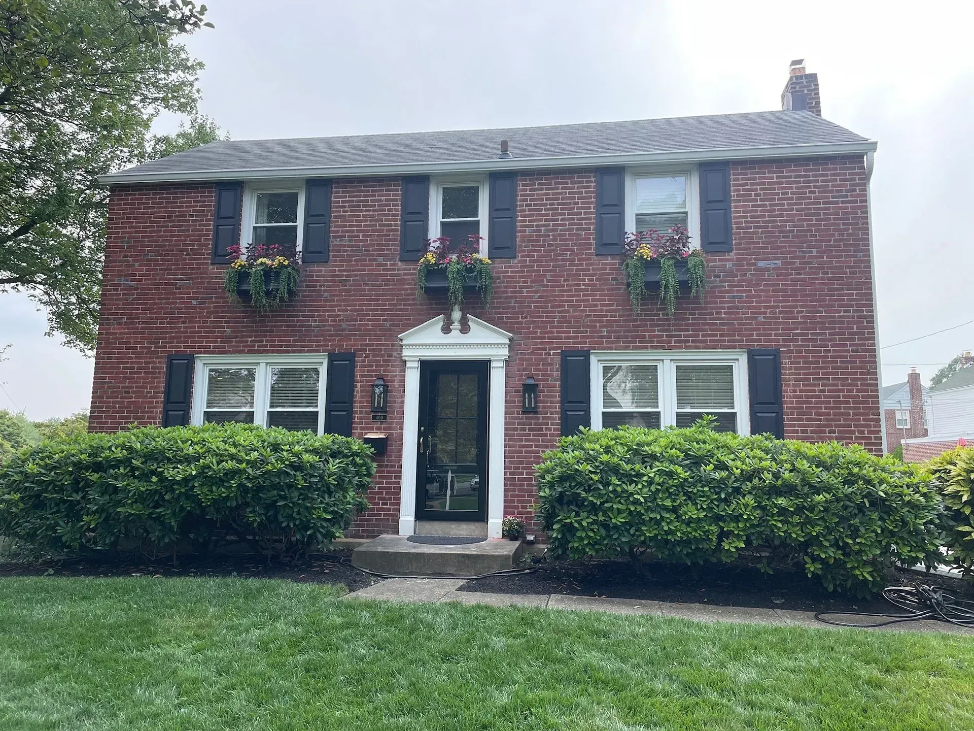 Red brick two-story house with black shutters, flower boxes, and a green lawn.