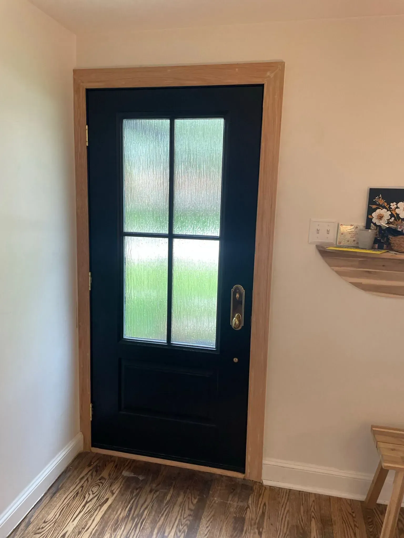 Black door with textured glass and light wood trim, in a white-walled room, next to a wooden side table.
