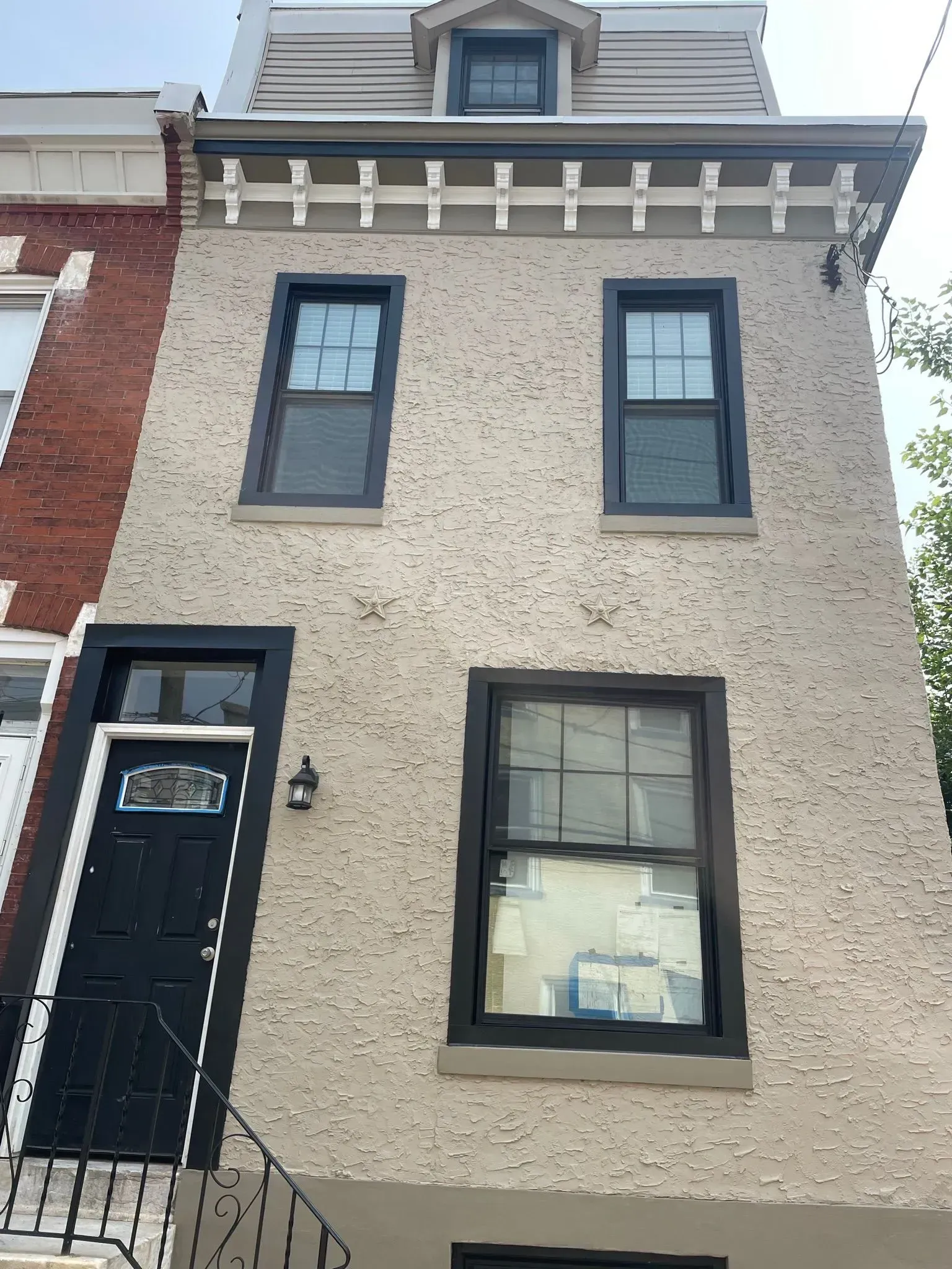 Tan stucco house with black framed windows and door. Decorative trim.