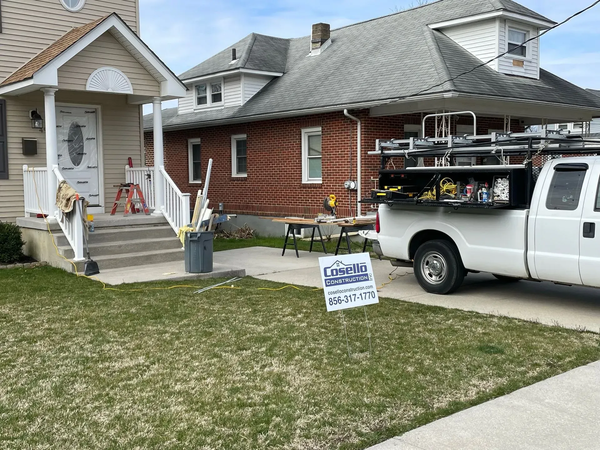White truck parked near house with workers, tools, and a sign.