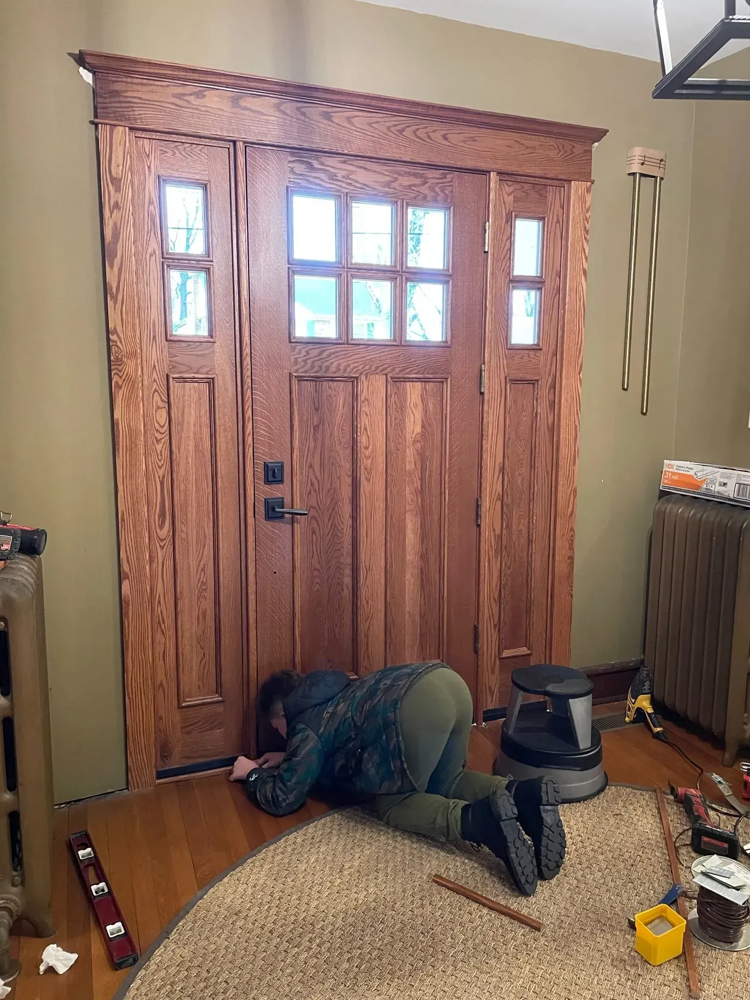 Person on floor, inspecting a wooden door with glass panels. Interior setting, visible tools.