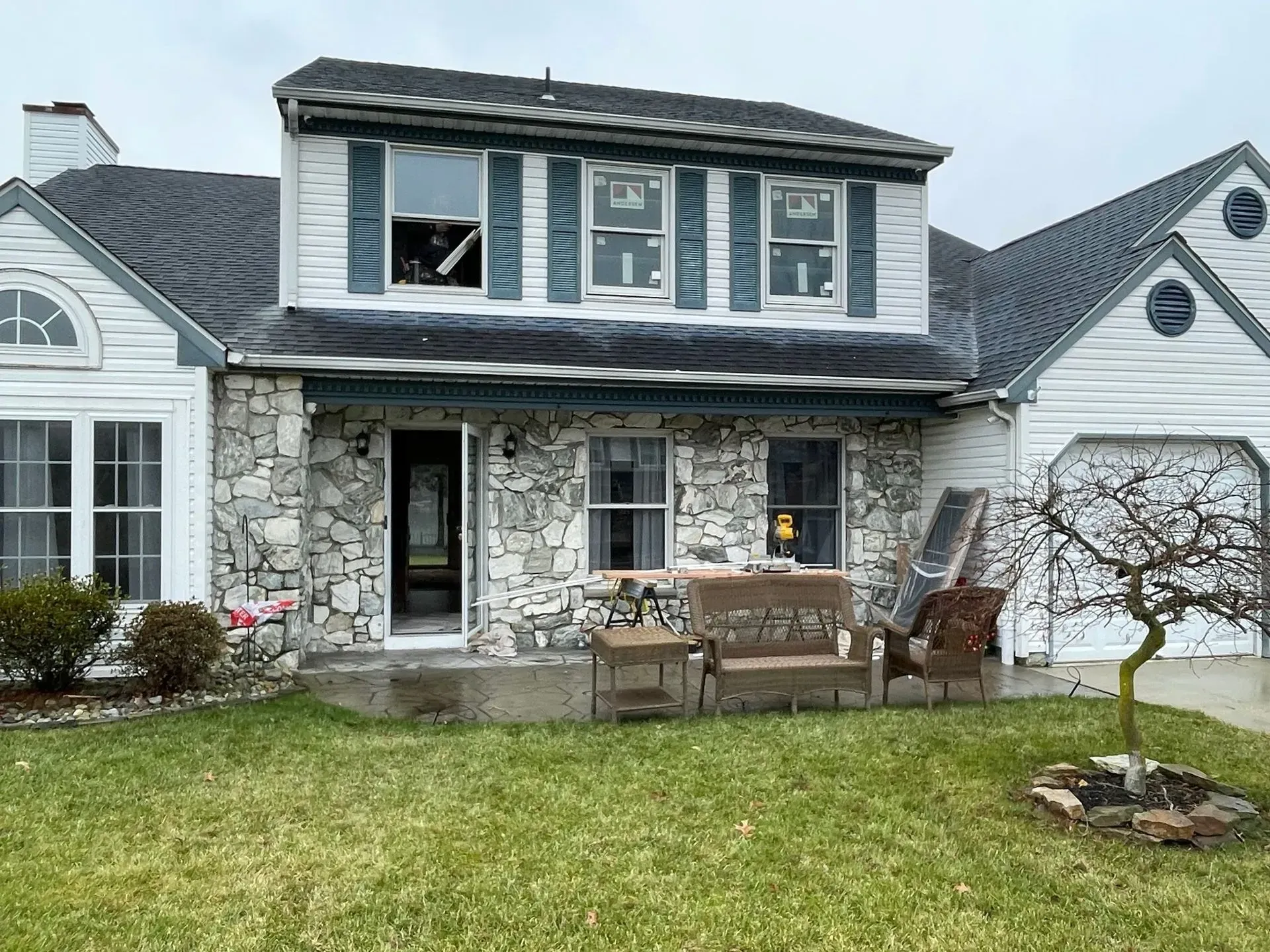 House with stone facade, damaged windows, and outdoor furniture on a cloudy day.