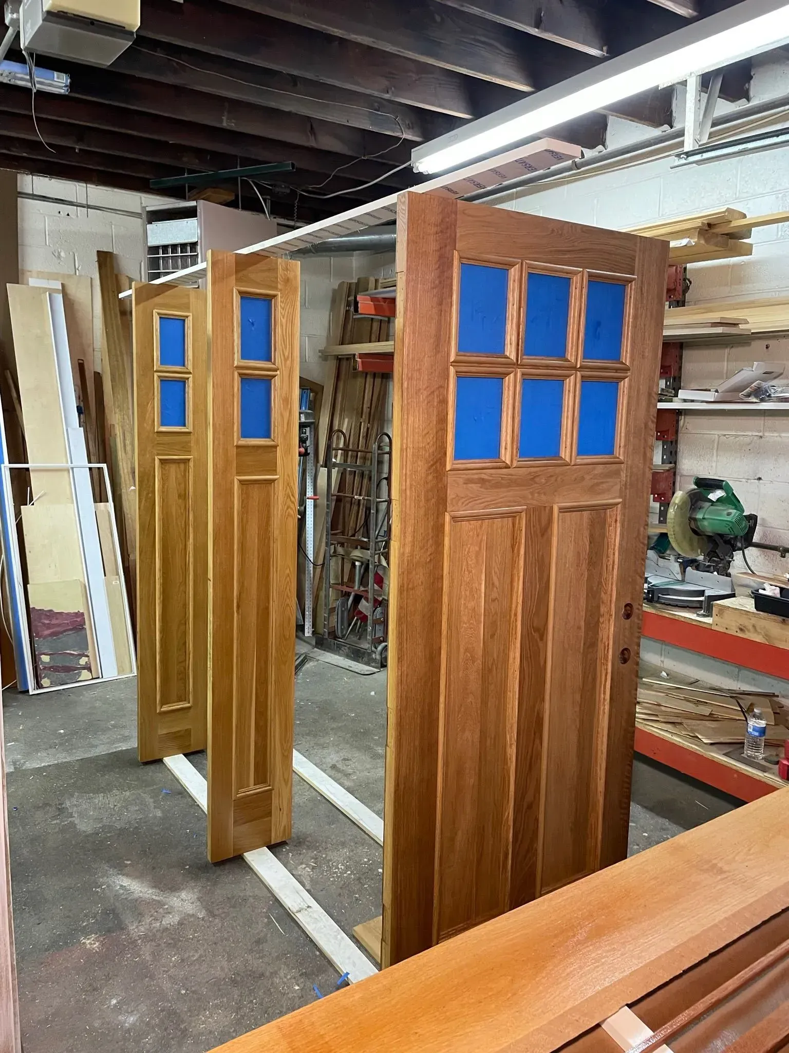 Three wooden doors with blue glass panes in a workshop setting.