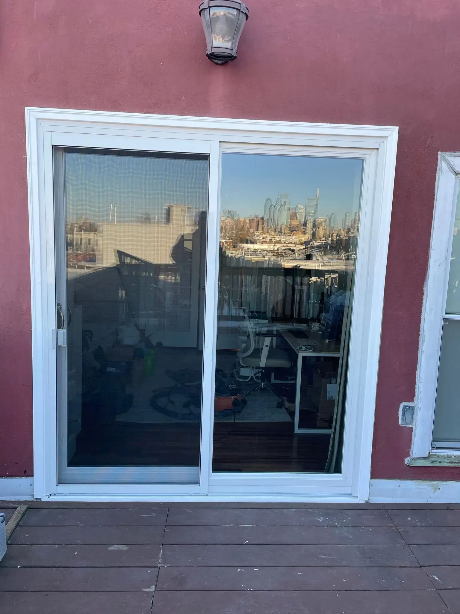 Sliding glass door with white frame on a red wall, reflecting a harbor view.