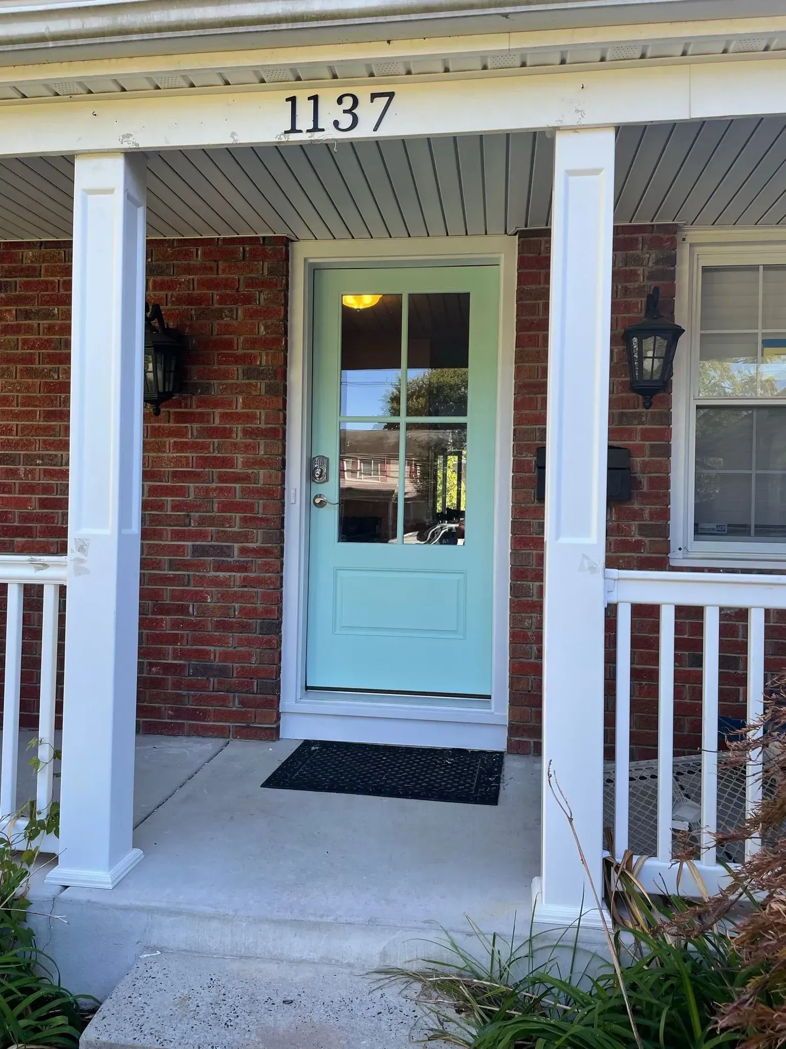 Front porch of a brick house with a teal door, white trim, and the number 1137 above.