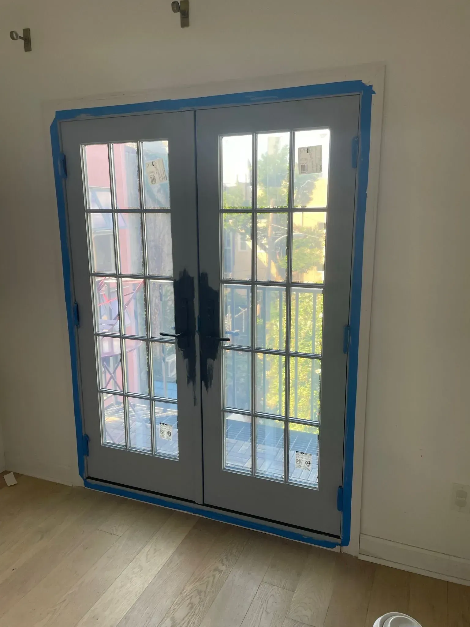 Double gray French doors with blue tape, inside a room with light wood floors.