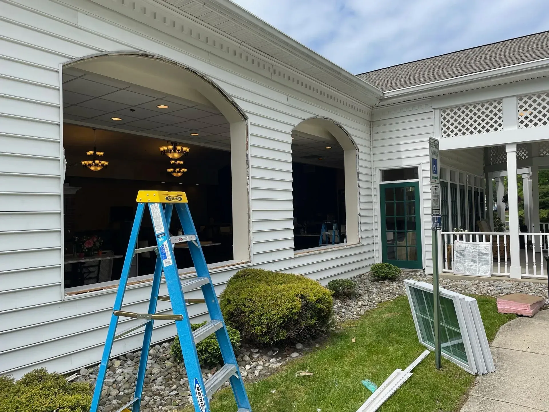 Building exterior with two large arched window openings, ladder, and window panes on the ground.