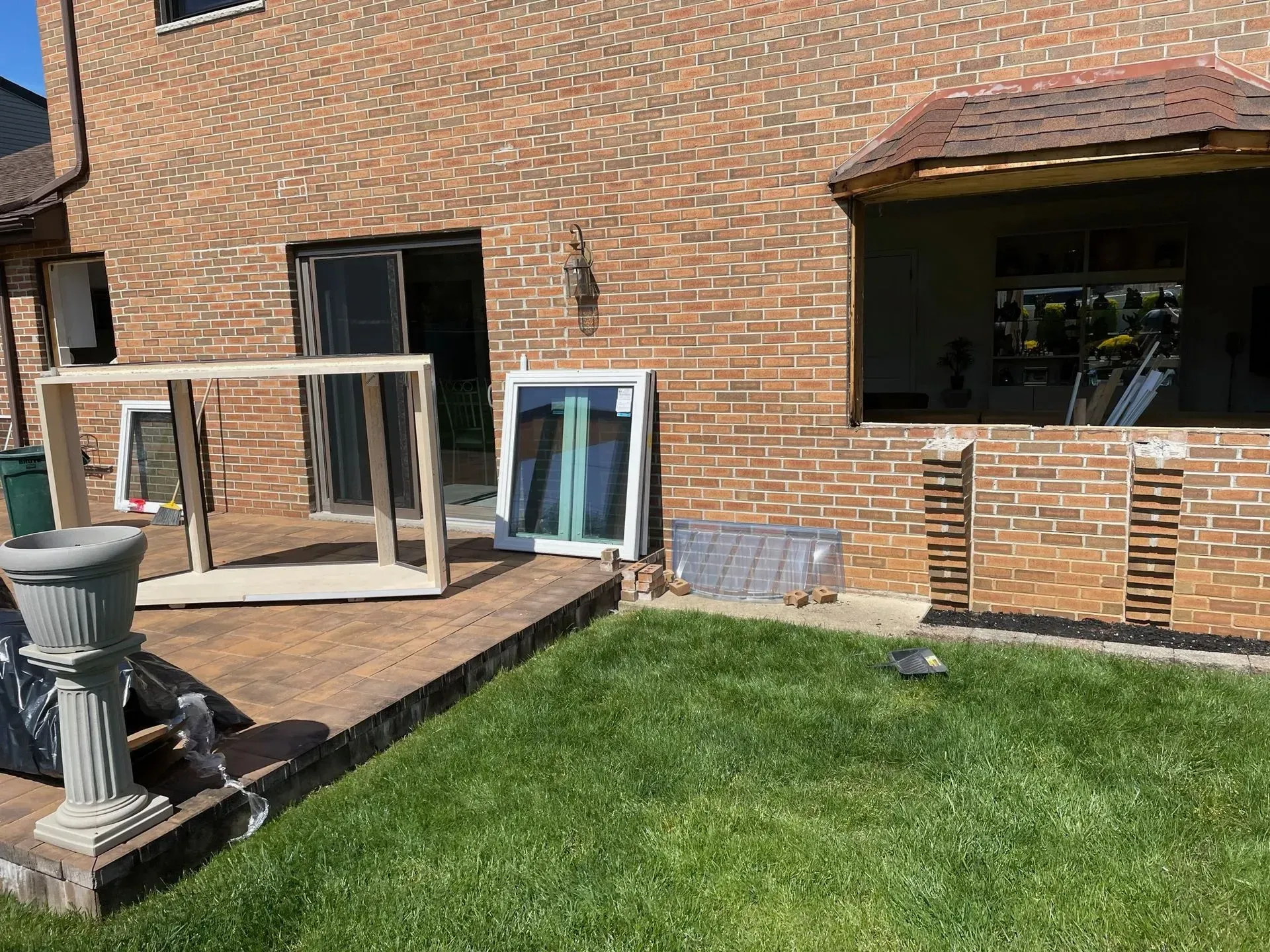 Backyard with brick house, wooden deck, replacement windows, and exposed wall during renovation.