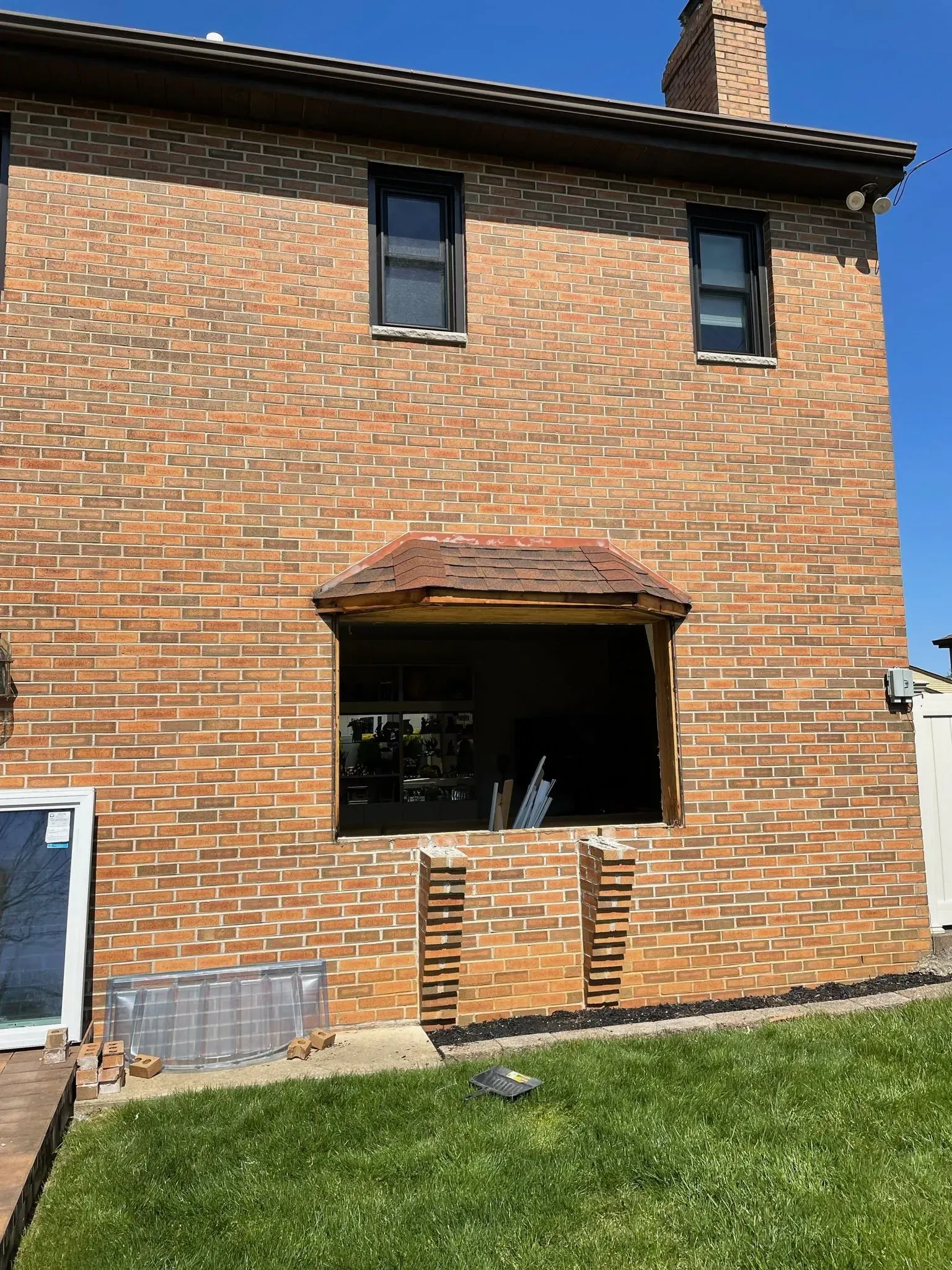 Brick house exterior with open window and roof. Two windows above, grass in foreground, blue sky.