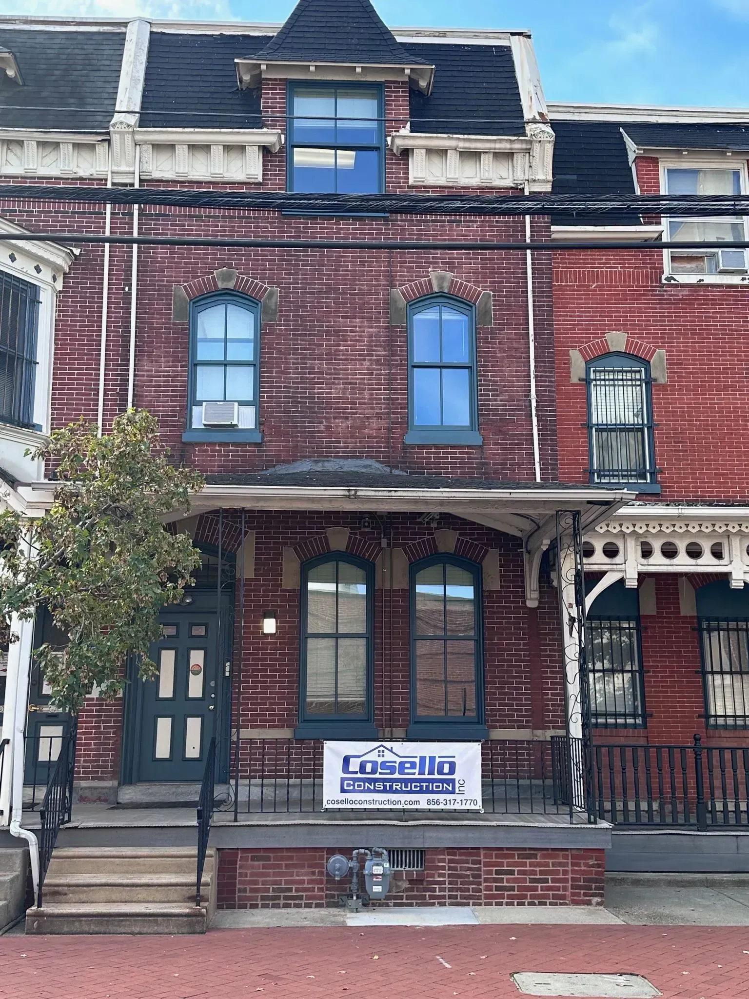 Red brick building with blue-framed windows, porch, and a sign that reads 