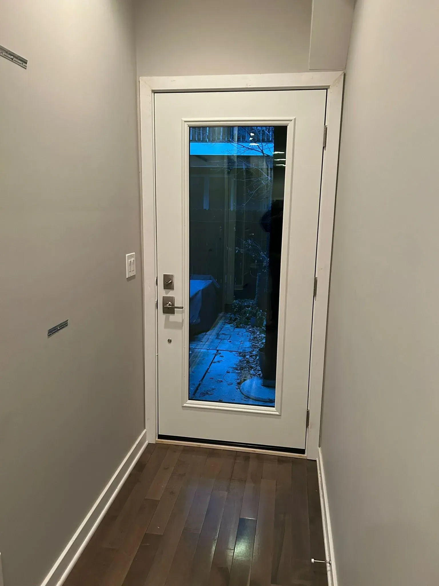 Hallway with a white door, glass is shattered, leading to an outdoor space.