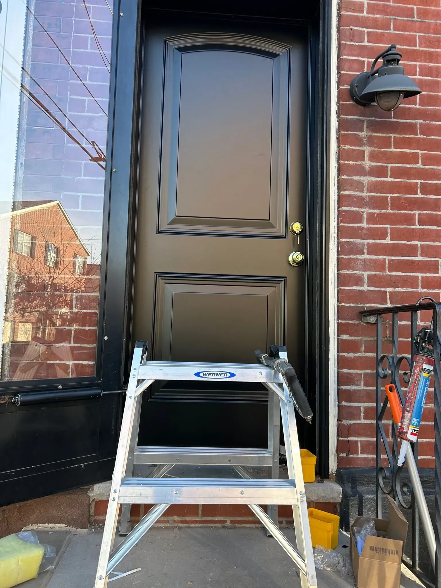 Black front door with a stepladder in front, on a brick building.