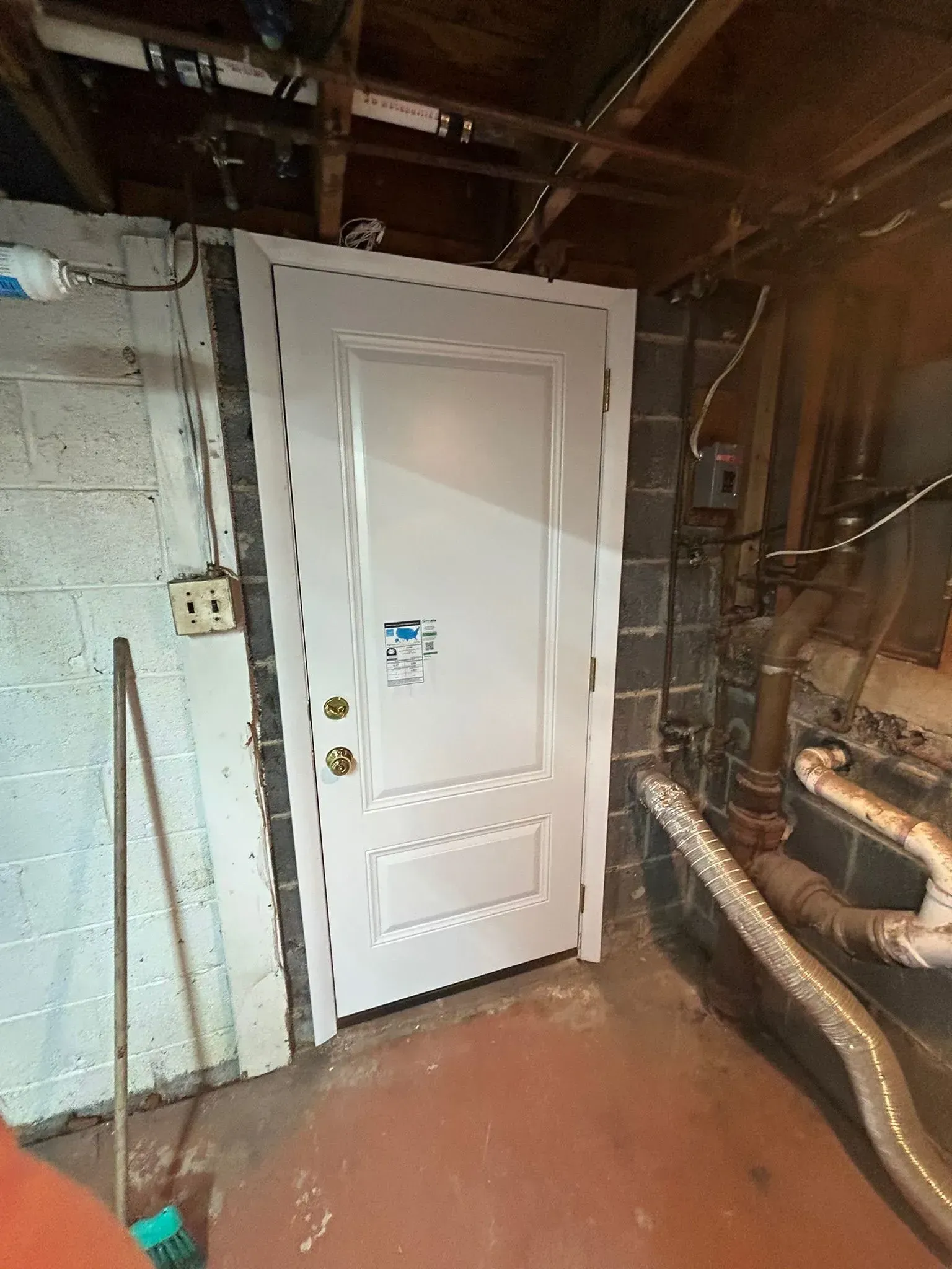 White door in a basement with cinder block walls and exposed pipes.