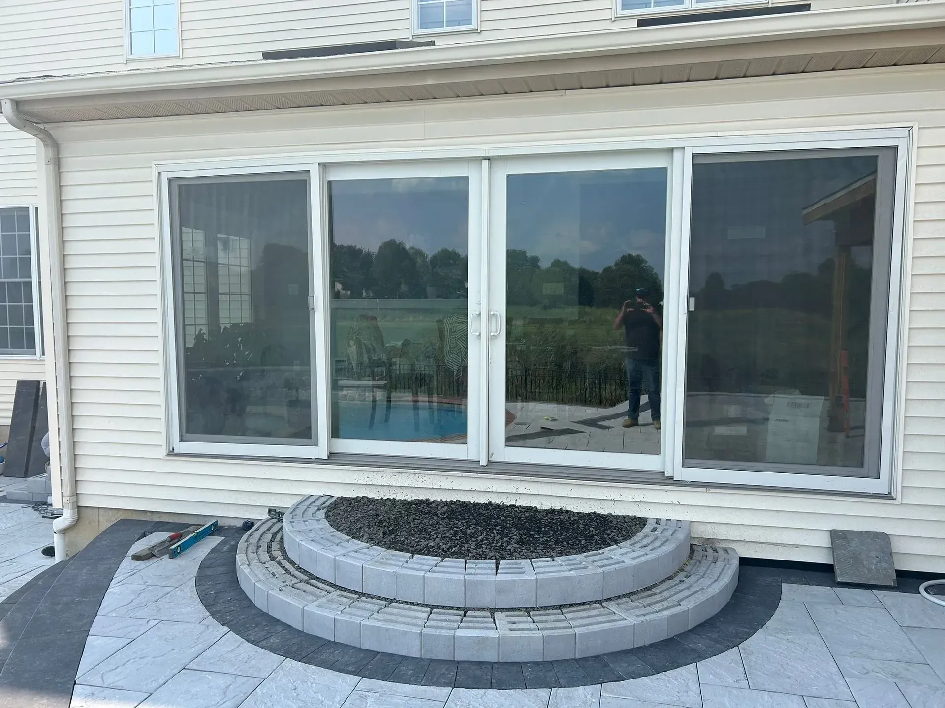 Sliding glass doors on a house open to a patio with a fire pit, overlooking a pool and field.
