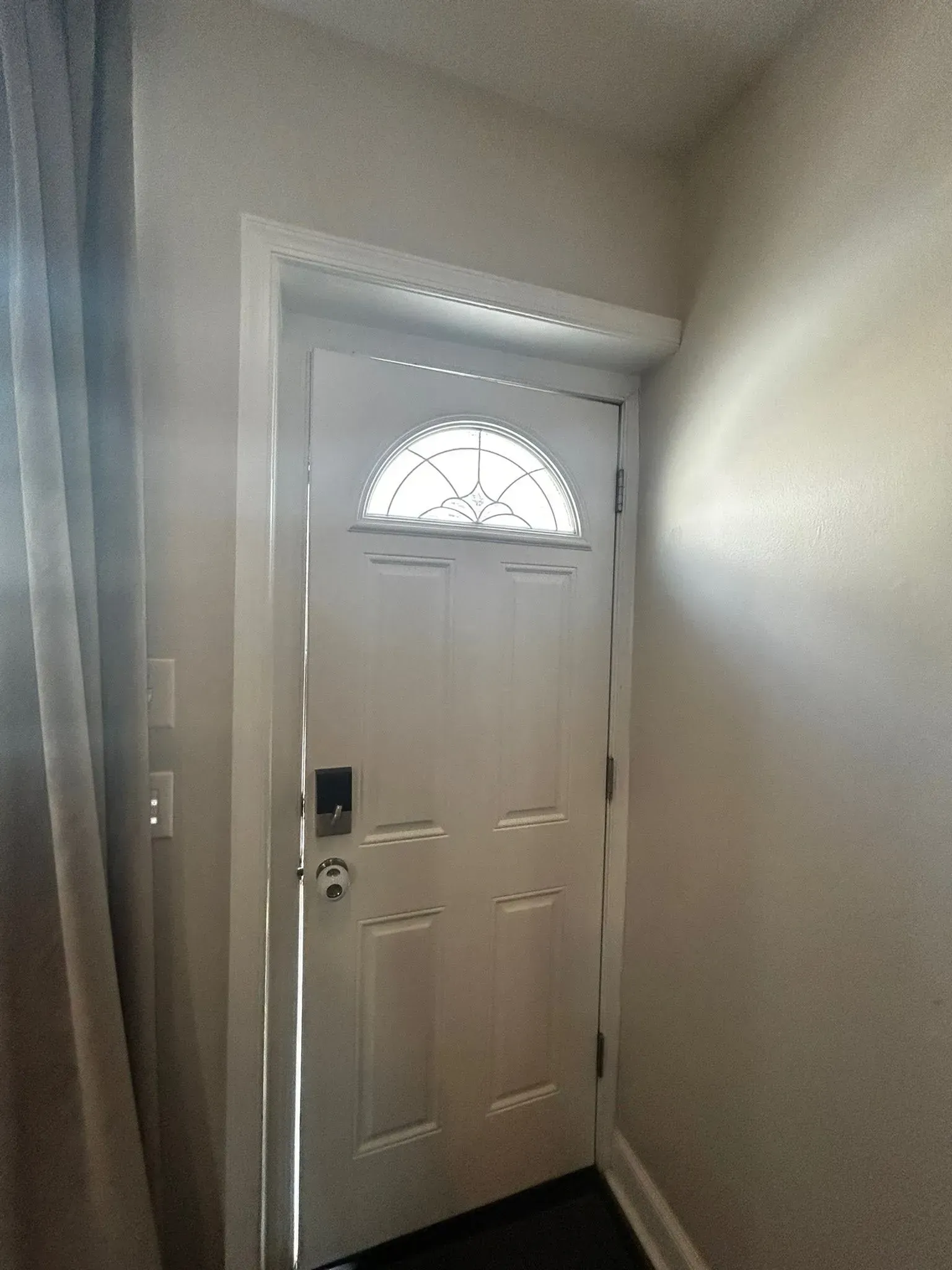 White front door with half-circle window and patterned trim. Sunlight streams in.