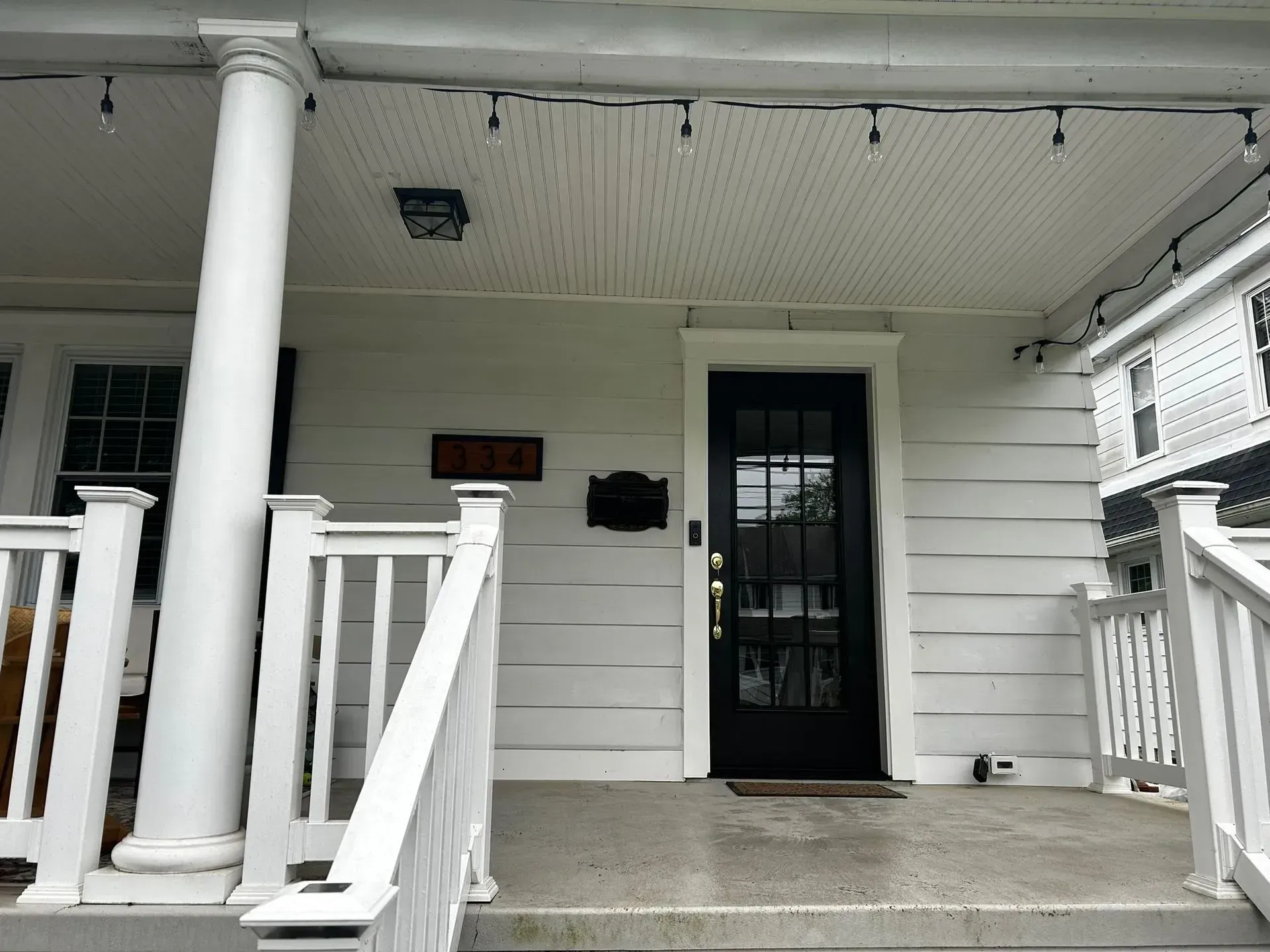 White porch with columns, a black door, and a house number plaque.