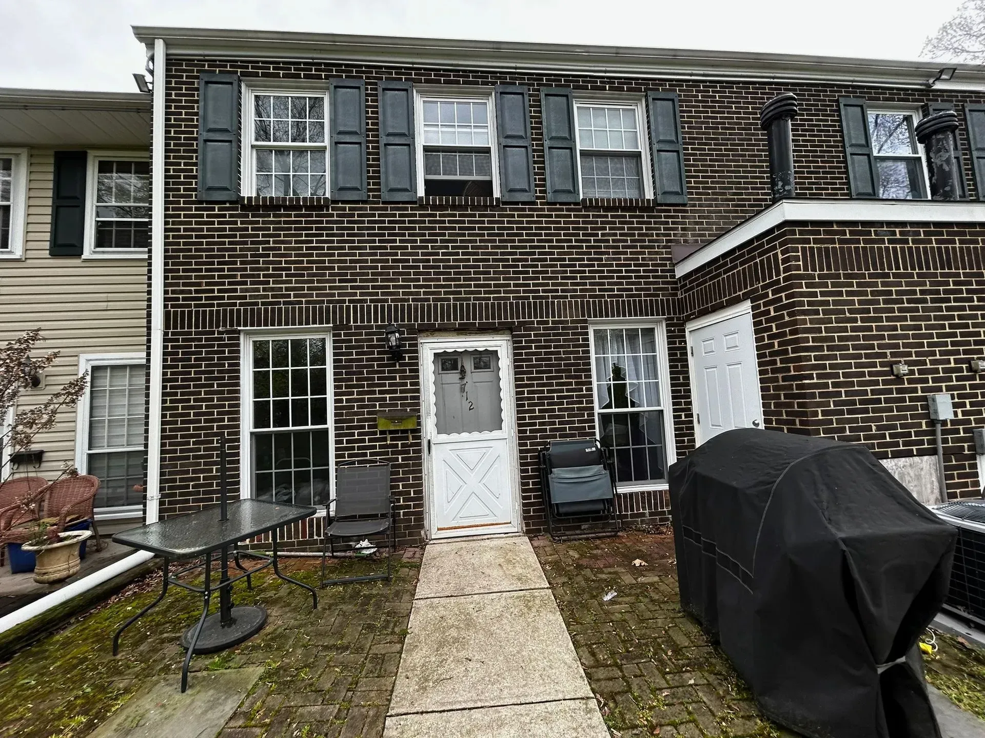 Brick townhouse with white door and windows, black shutters. Patio with table, chairs, grill.