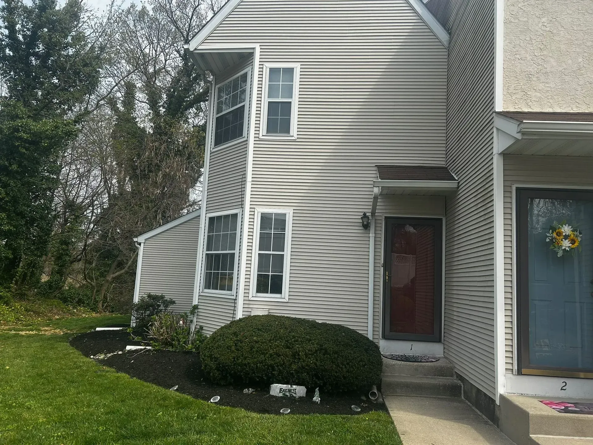 Two-story townhouse with beige siding, red door, and landscaping, next to another similar unit.