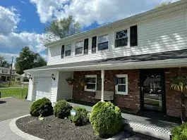 Two-story white house with brick facade, black shutters, and garage, under a blue cloudy sky.