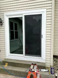 Sliding glass door with screen, white trim, on a concrete step. A ladder and caulk gun are below.