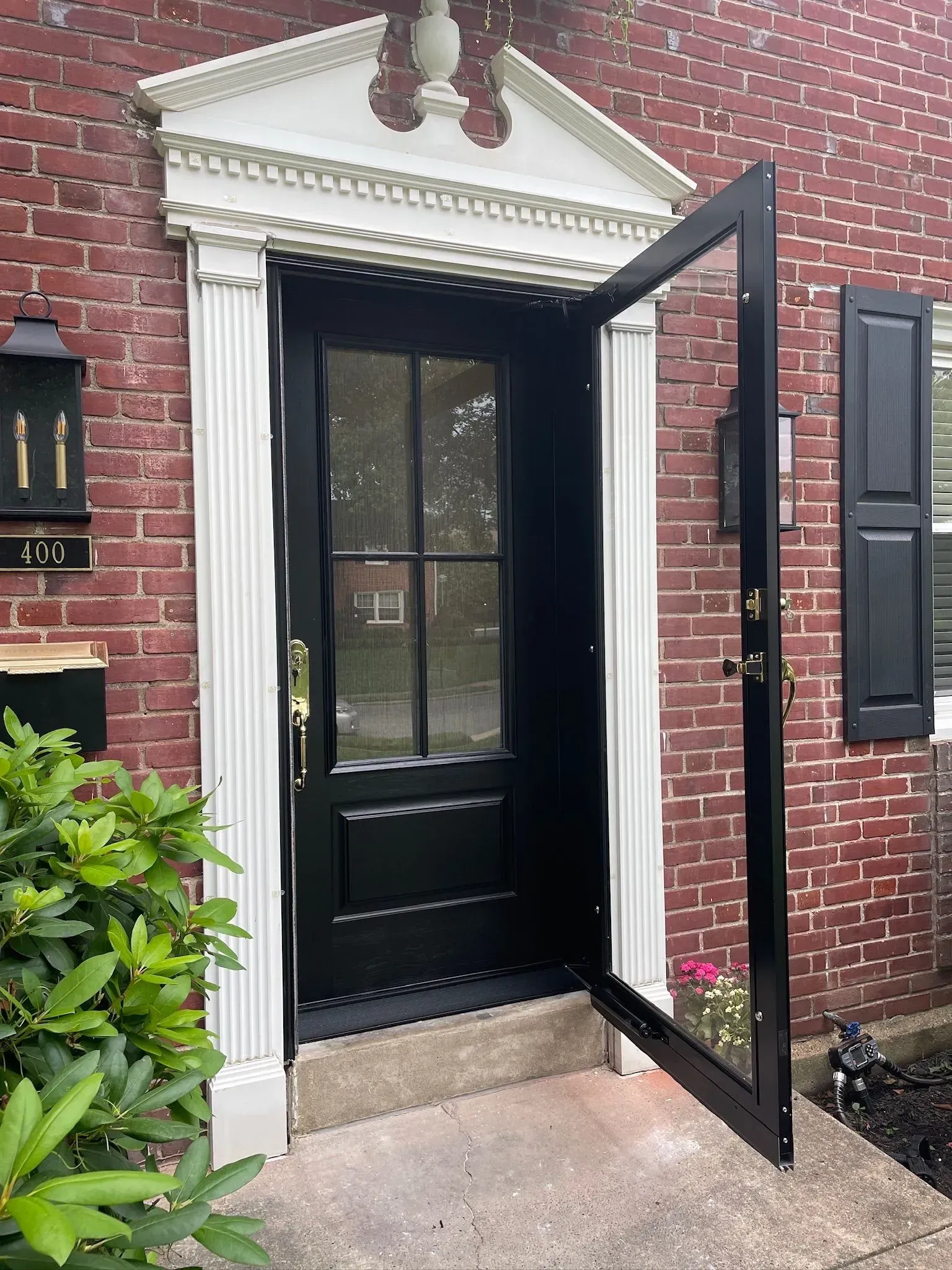 Black front door with open screen door, white trim, brick exterior.