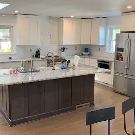 Modern kitchen remodel with white cabinets, dark island, and stainless steel appliances.