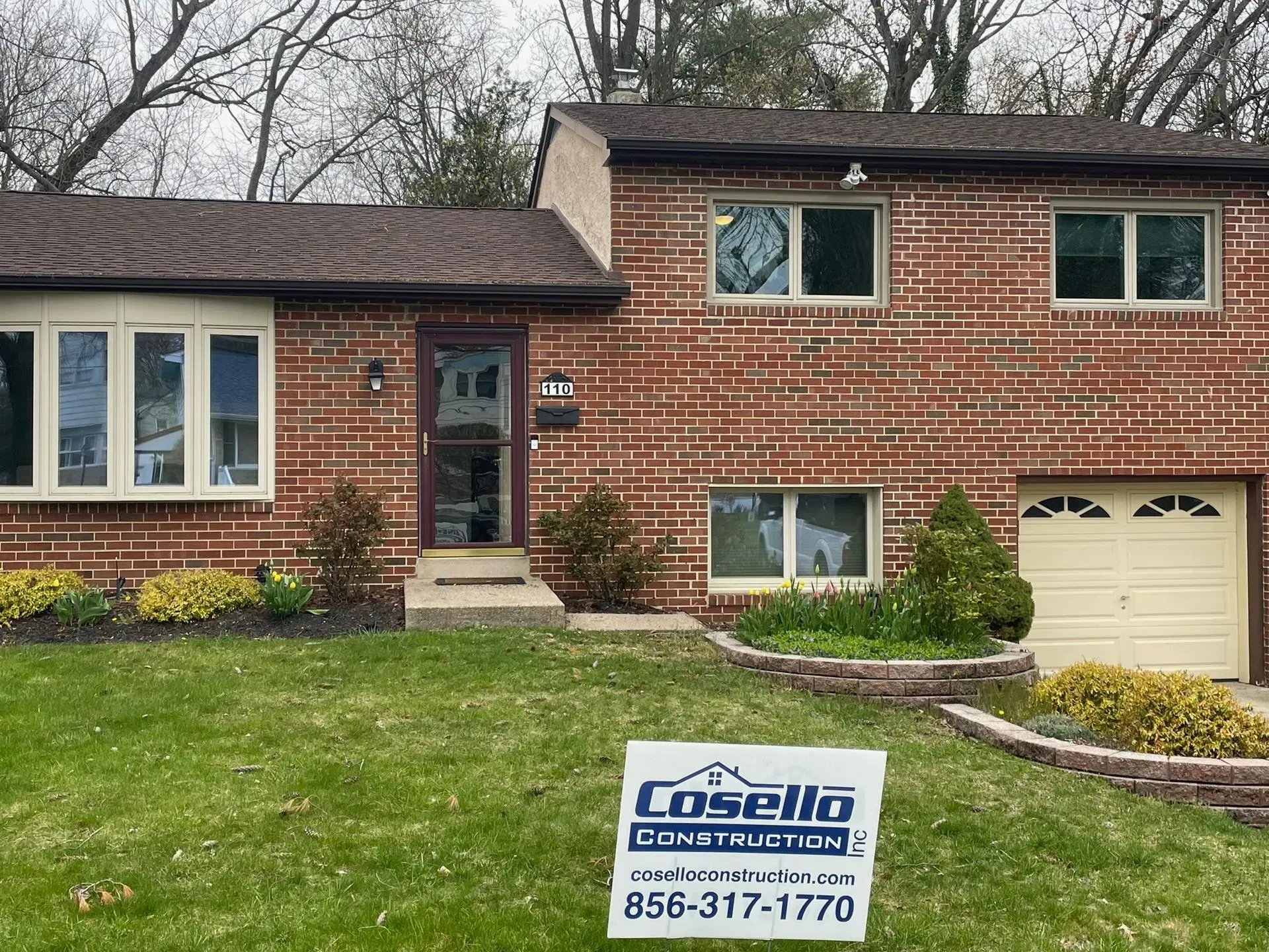 A brick house with a brown roof and a sign for Casello Construction in the yard.