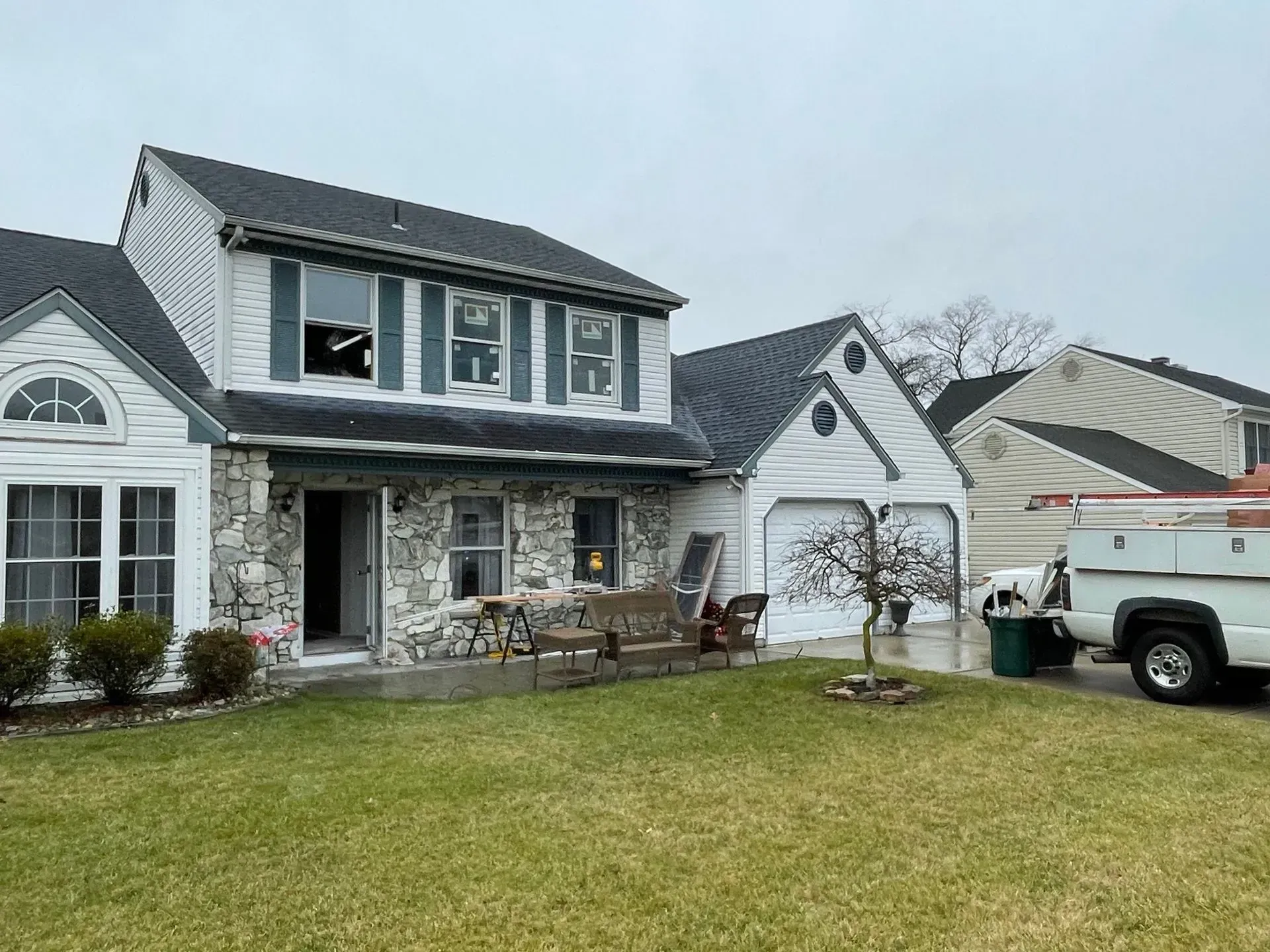 Two-story white house with stone facade, two-car garage, and green lawn. A white truck is parked nearby.