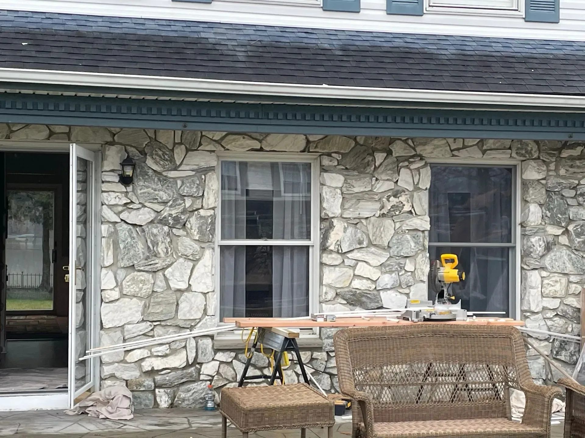 Exterior of a stone-walled house with windows and a door open. A saw sits outside a window.