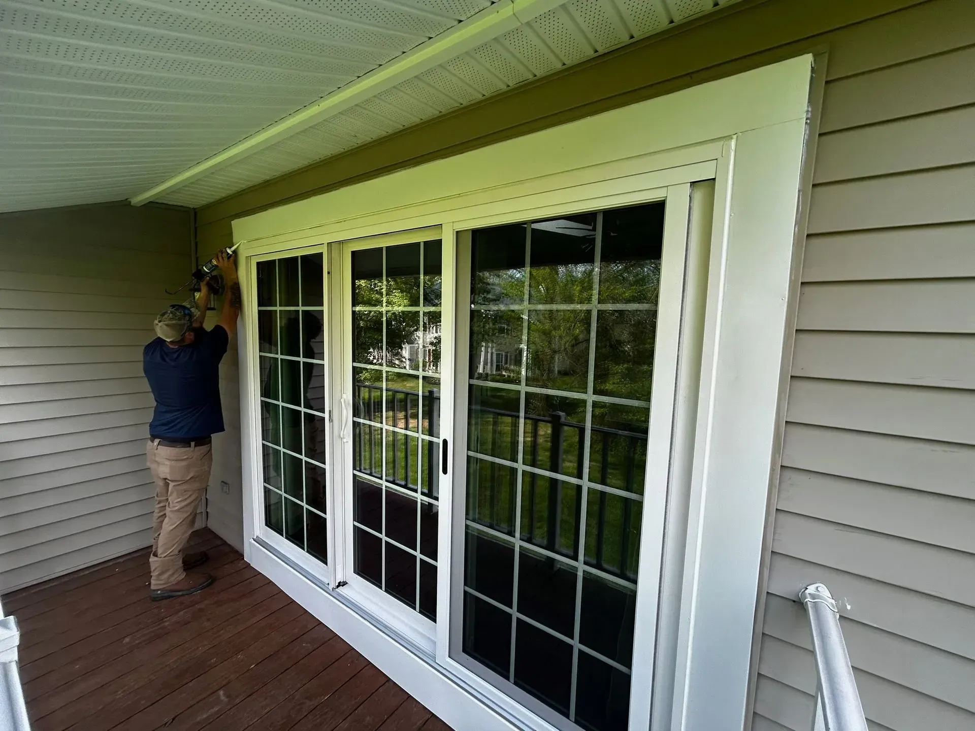 Person installing trim around white sliding glass doors on a porch with beige siding.