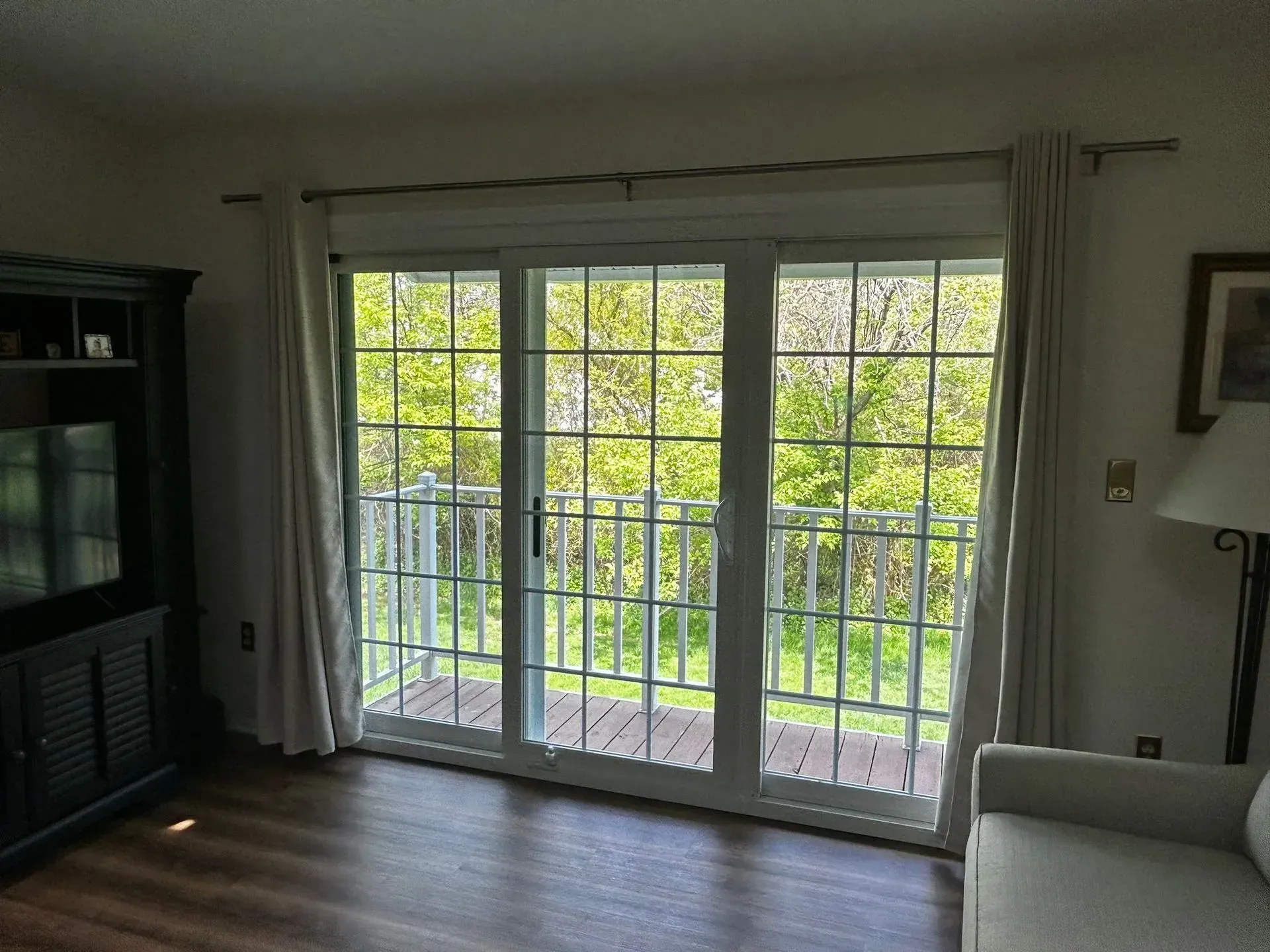 Sliding glass doors open onto a balcony with trees visible. Curtains and furniture flank the doors.
