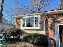 House exterior with a bay window, American flag, and bushes.
