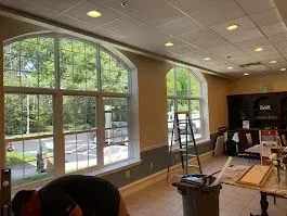 Interior of a building with arched windows, one large, showing outdoor view. Person works near the windows.