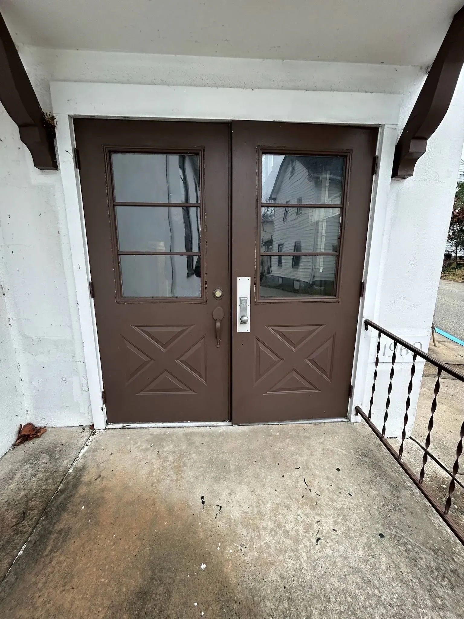 Brown double doors with glass panels and a decorative X pattern, set in a white stucco frame, with a concrete landing.