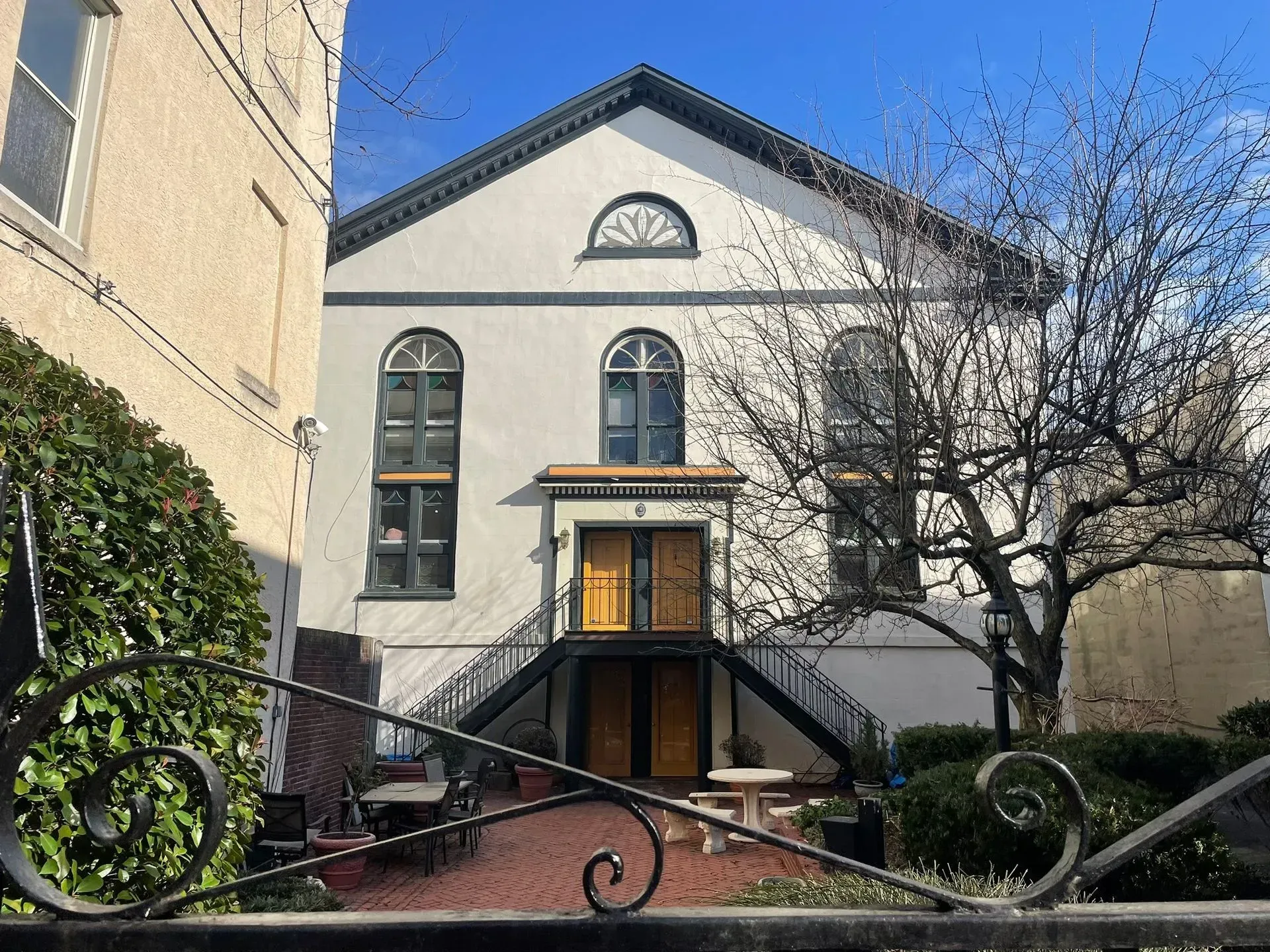 White building with arched windows, double yellow doors, and black metal staircase.