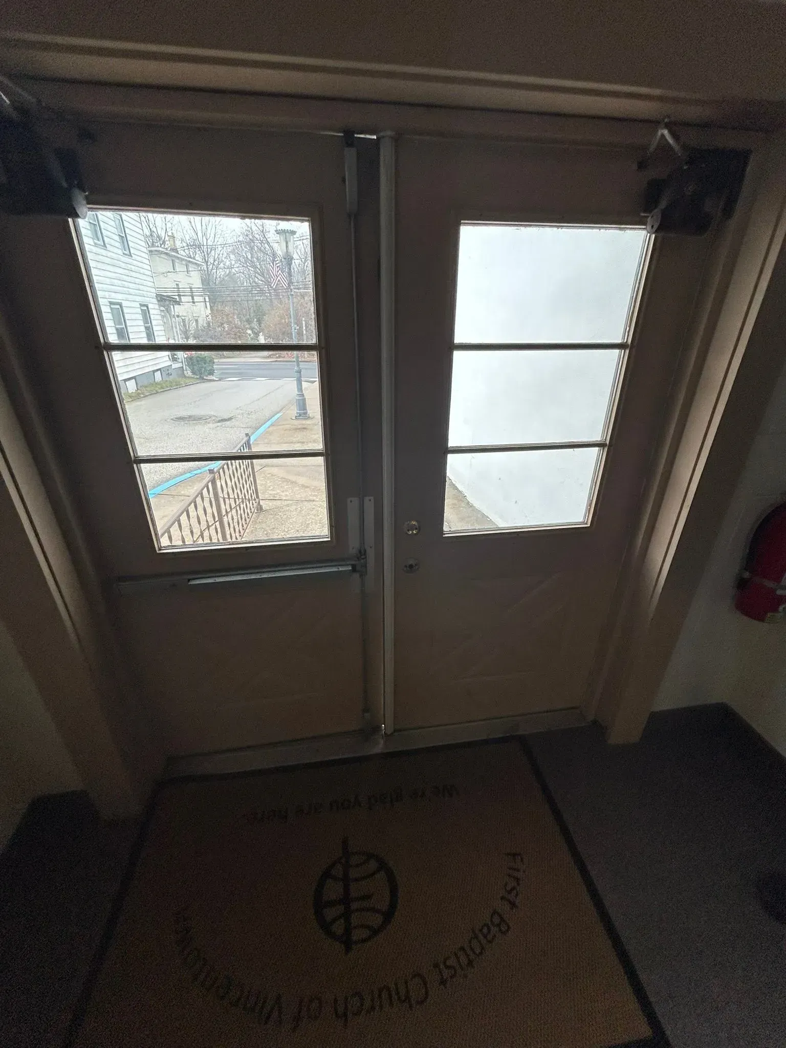 Two wooden doors with glass panels; doormat in front.