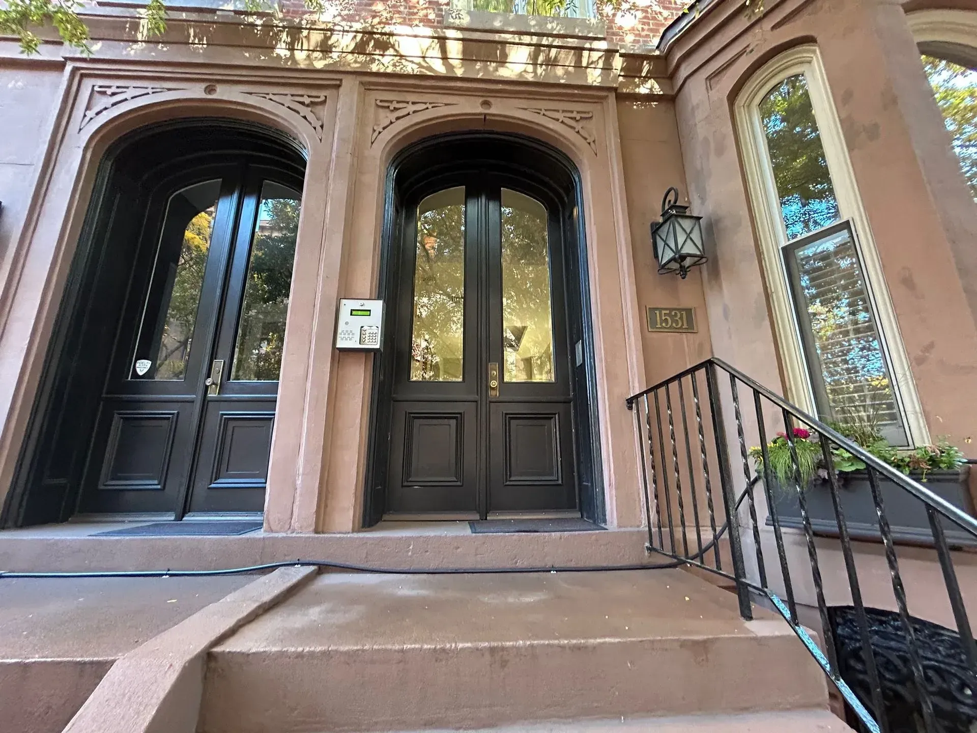 Brownstone building with arched black doors, steps, and wrought iron railing.