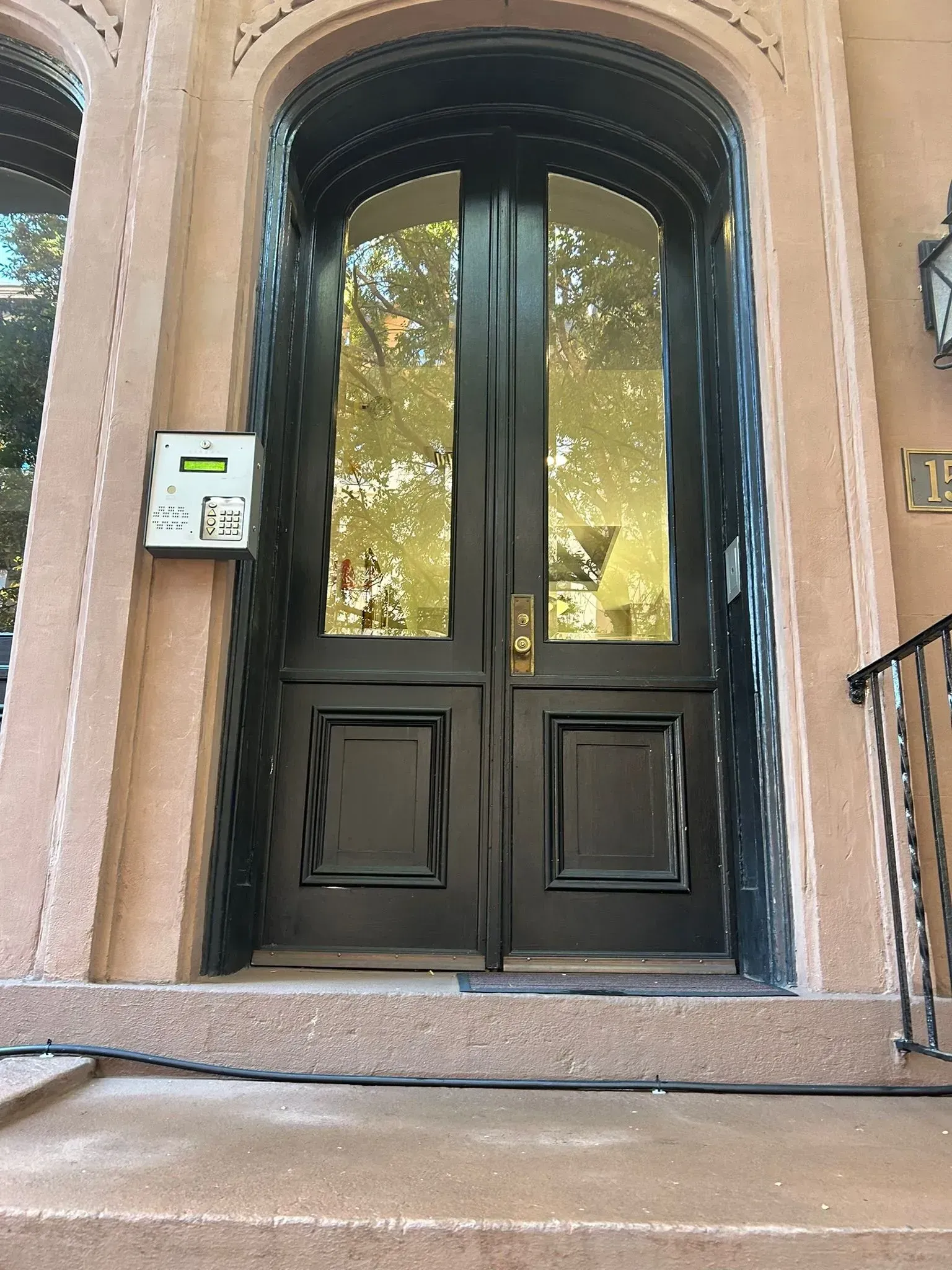 Black double doors with arched tops and glass panels, in a brownstone building entrance.