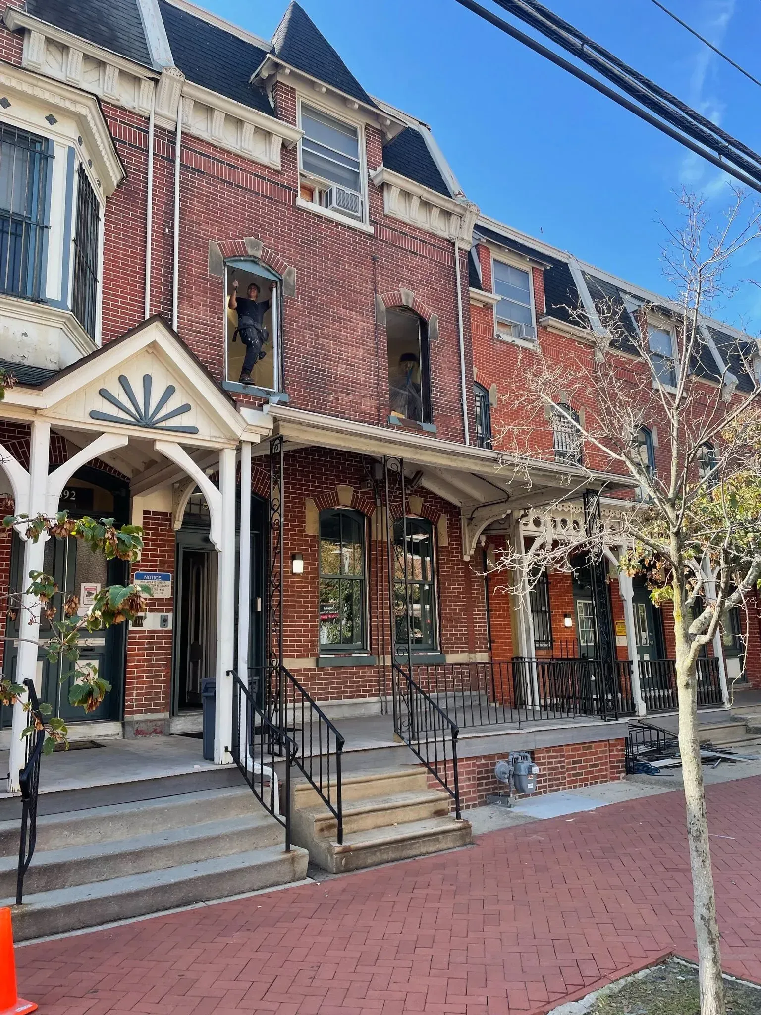 Row of brick townhouses with ornate porches and black wrought iron details; red brick street.