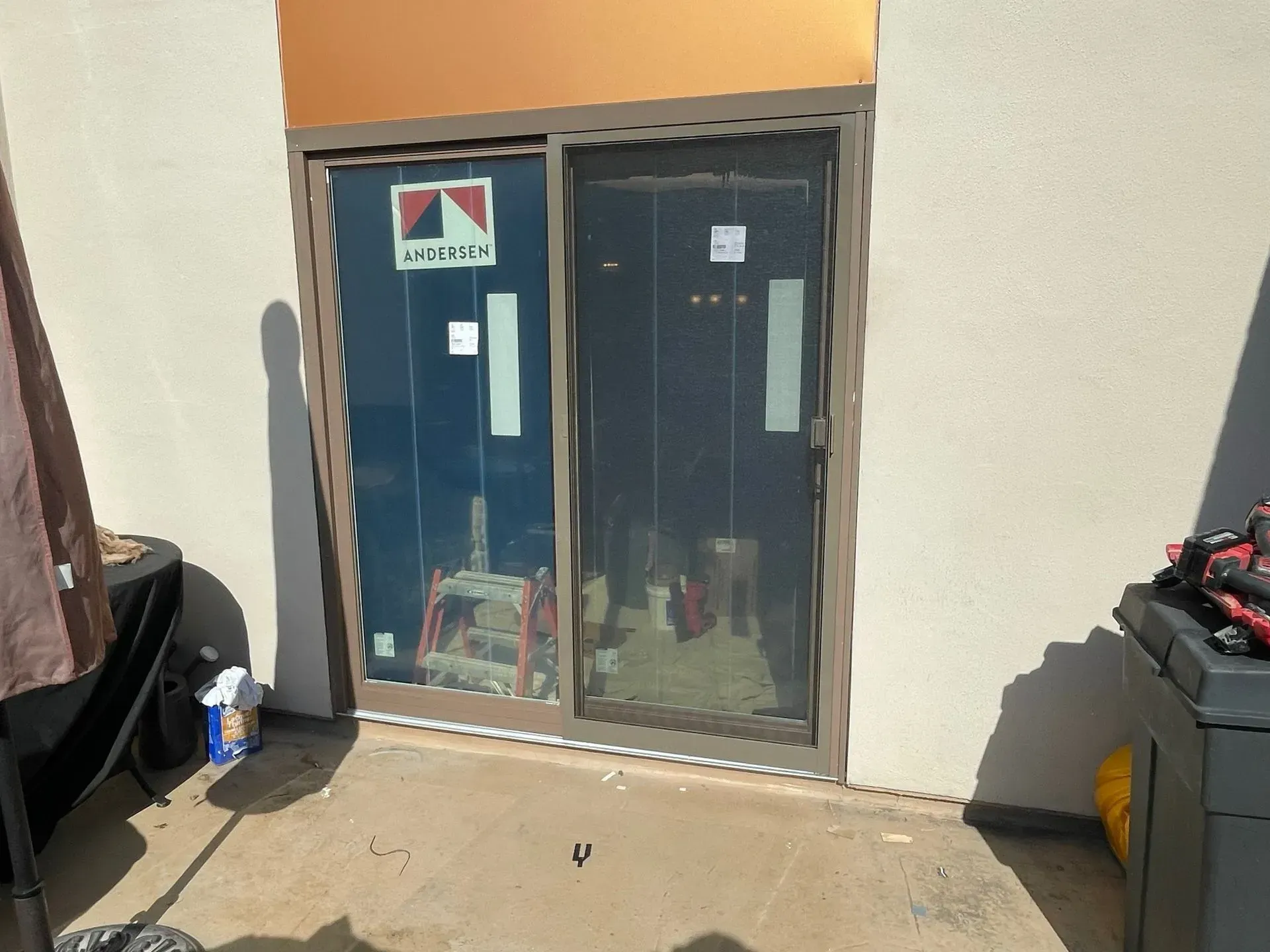 Sliding glass door on a concrete patio. The door is framed by light brown. Objects and a patio set are nearby.