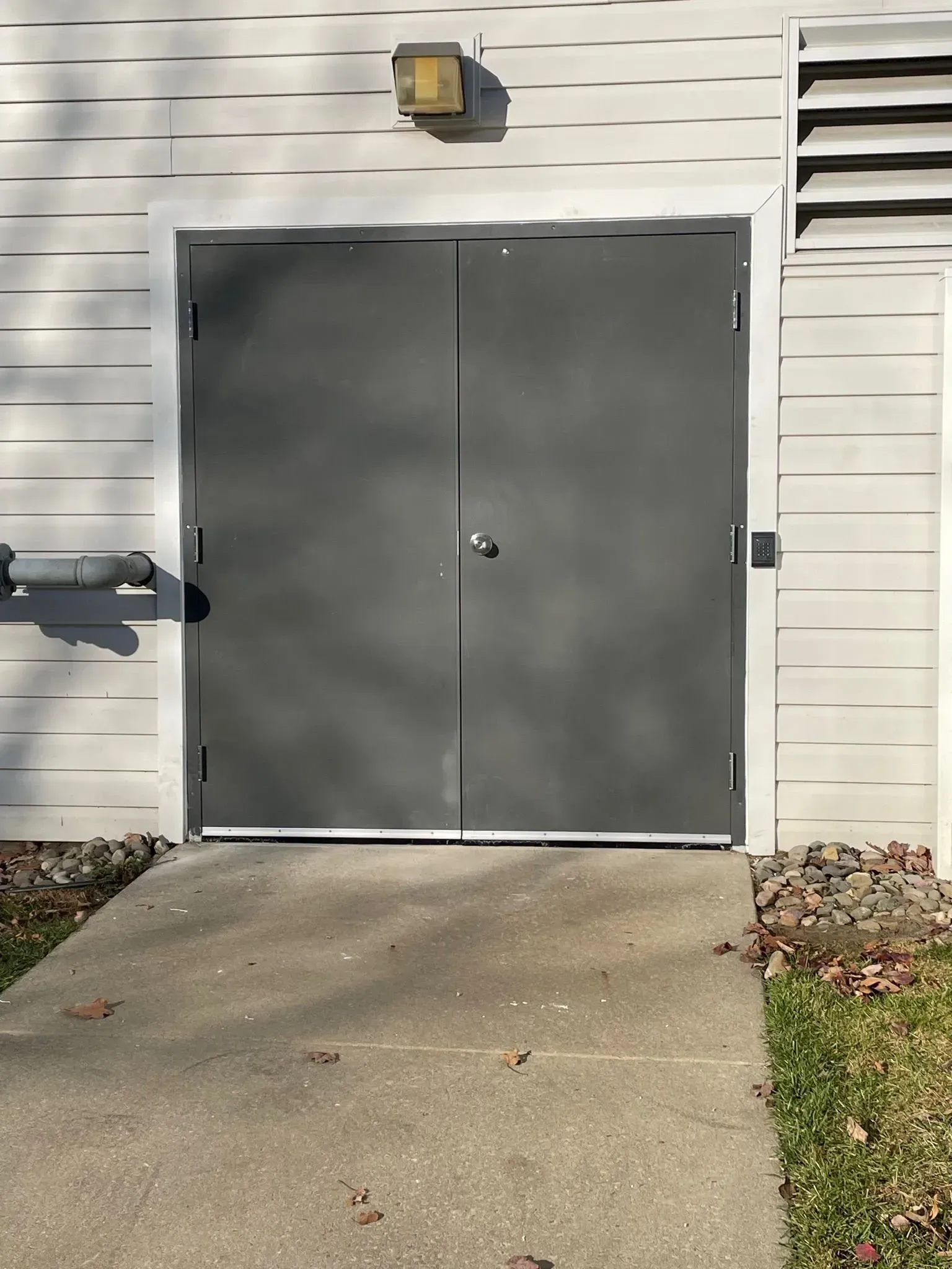 Gray double doors on a building, a concrete ramp leads to the entrance.