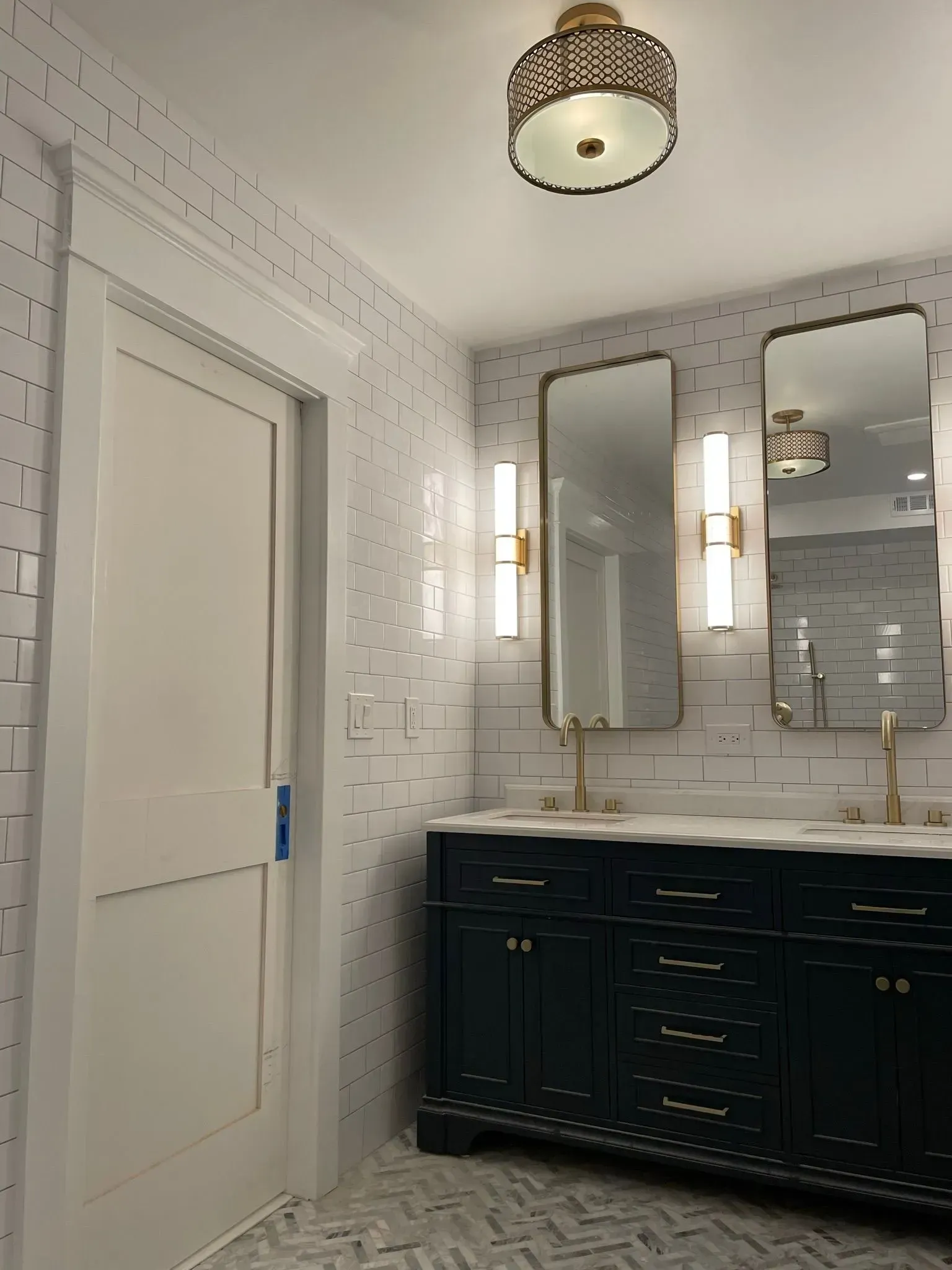 Bathroom with teal vanity, gold accents, white tile walls, and two large mirrors.