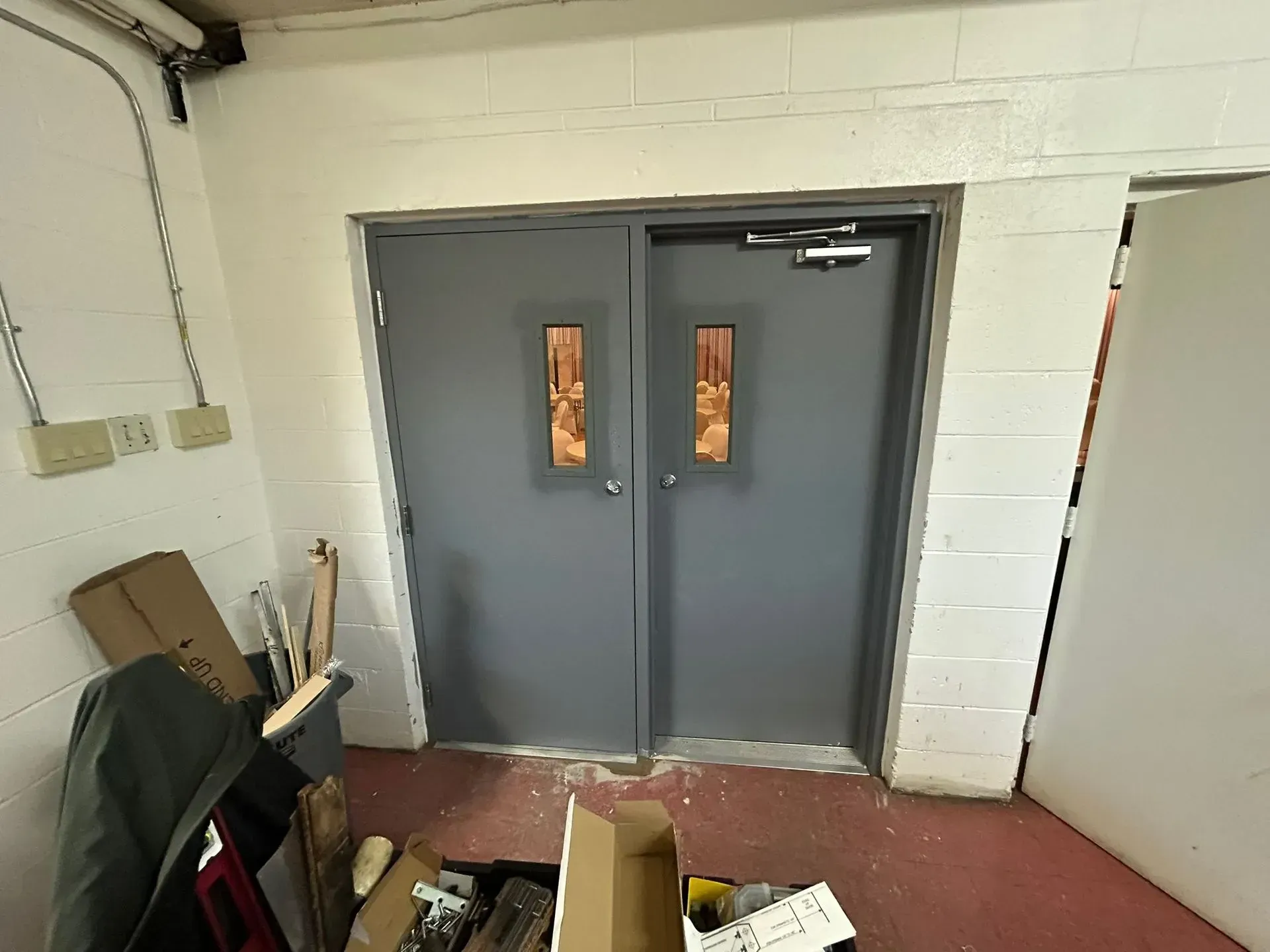 Gray double doors with copper accents in a white-walled room, cluttered with boxes and tools.