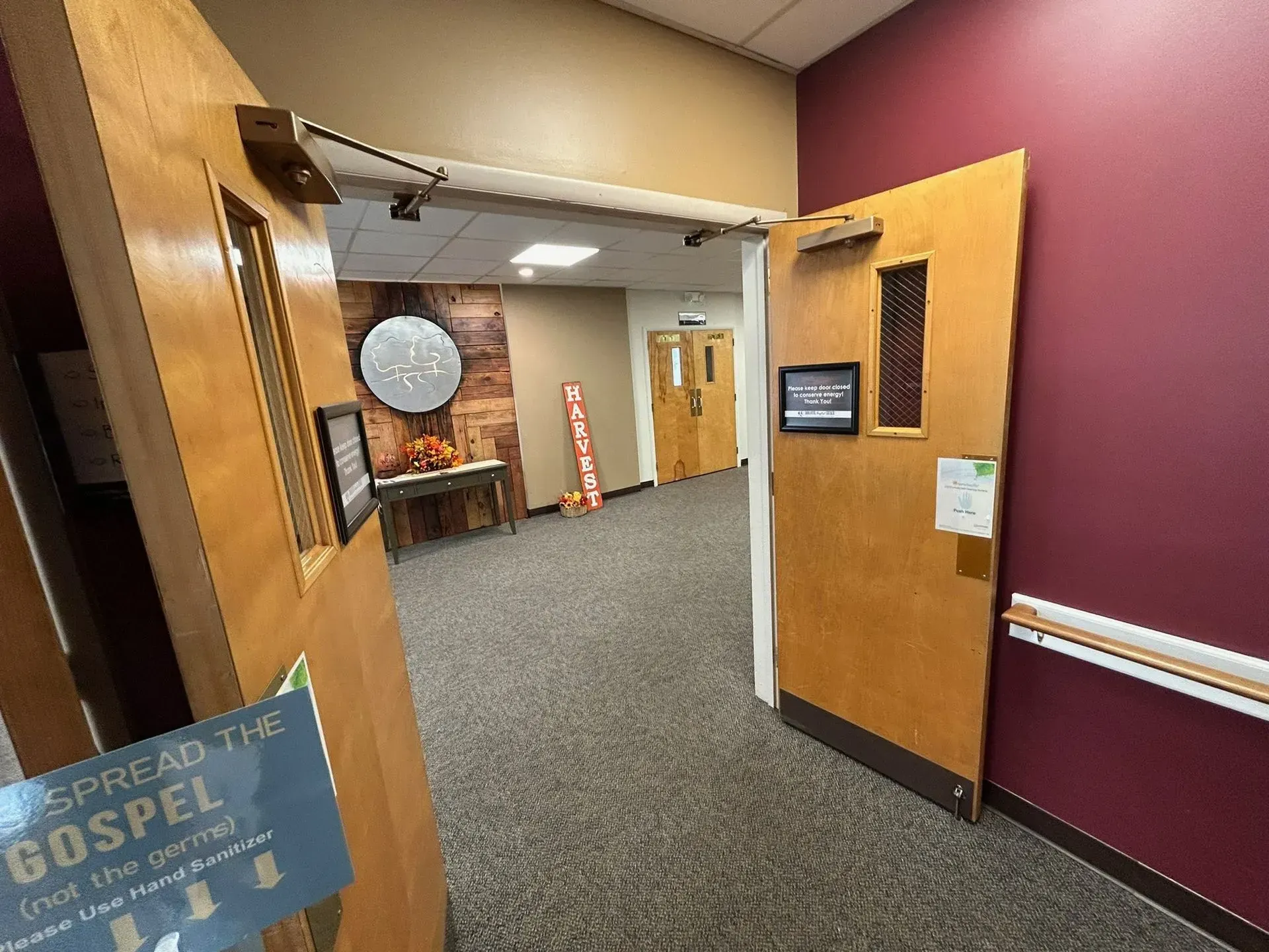 Doors open to a hallway with a table, signs, and a doorway. Dark carpet and maroon wall.