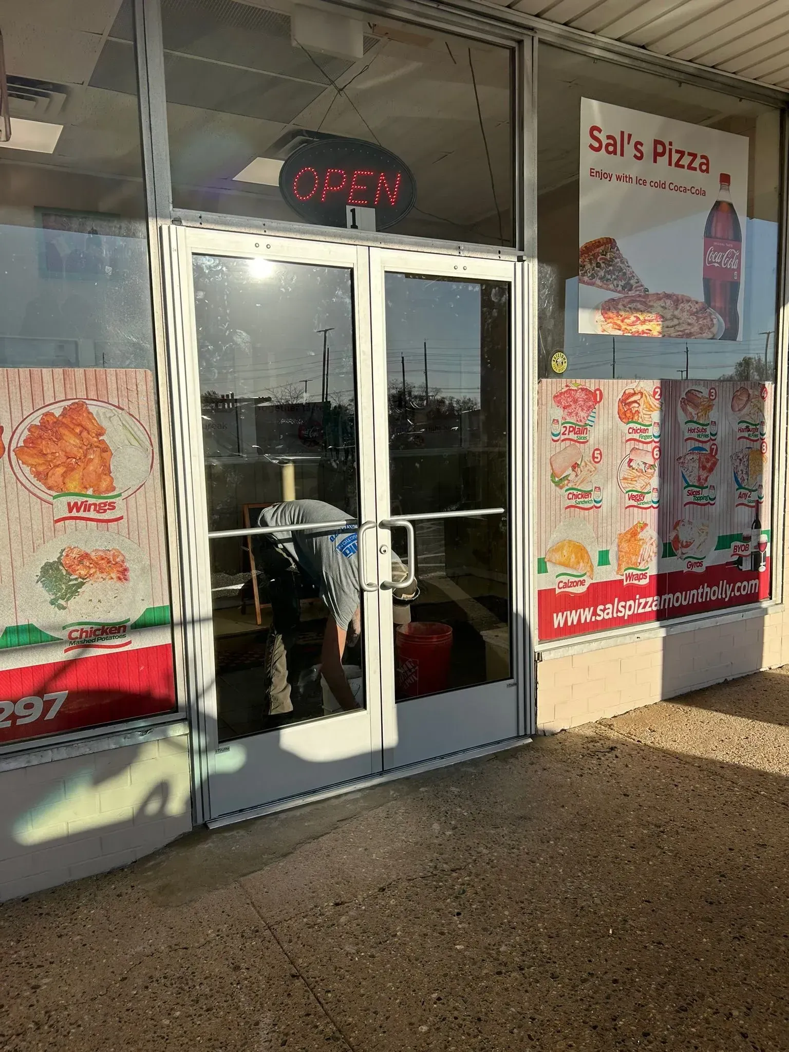 Exterior of Sal's Pizza restaurant with glass door. Sunlight reflects off the glass. Menu posters are on the windows.